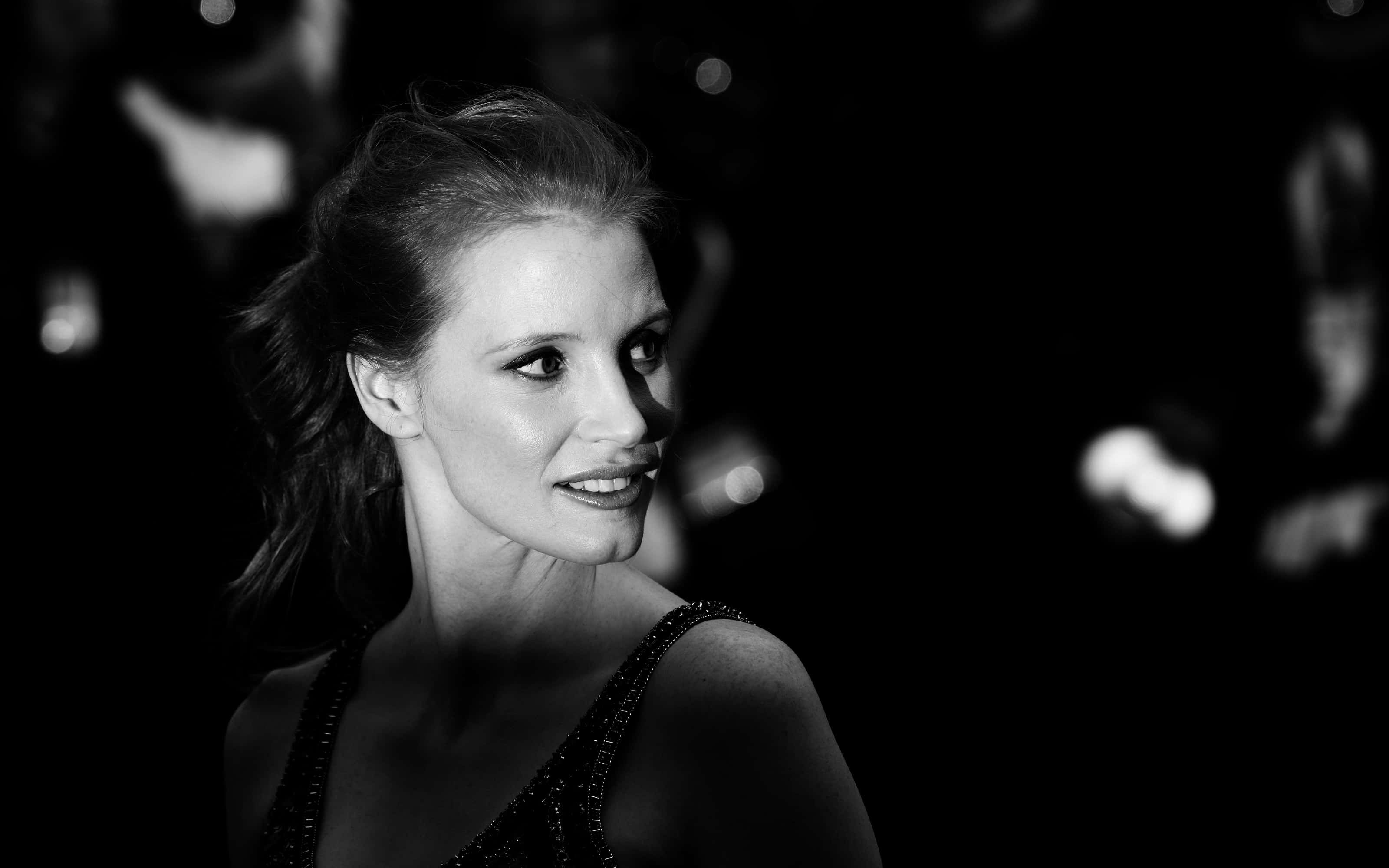 jessica chastain 桌布 壁紙 — 一位女士的黑白肖像，背景有模糊的燈光，她溫柔地微笑。