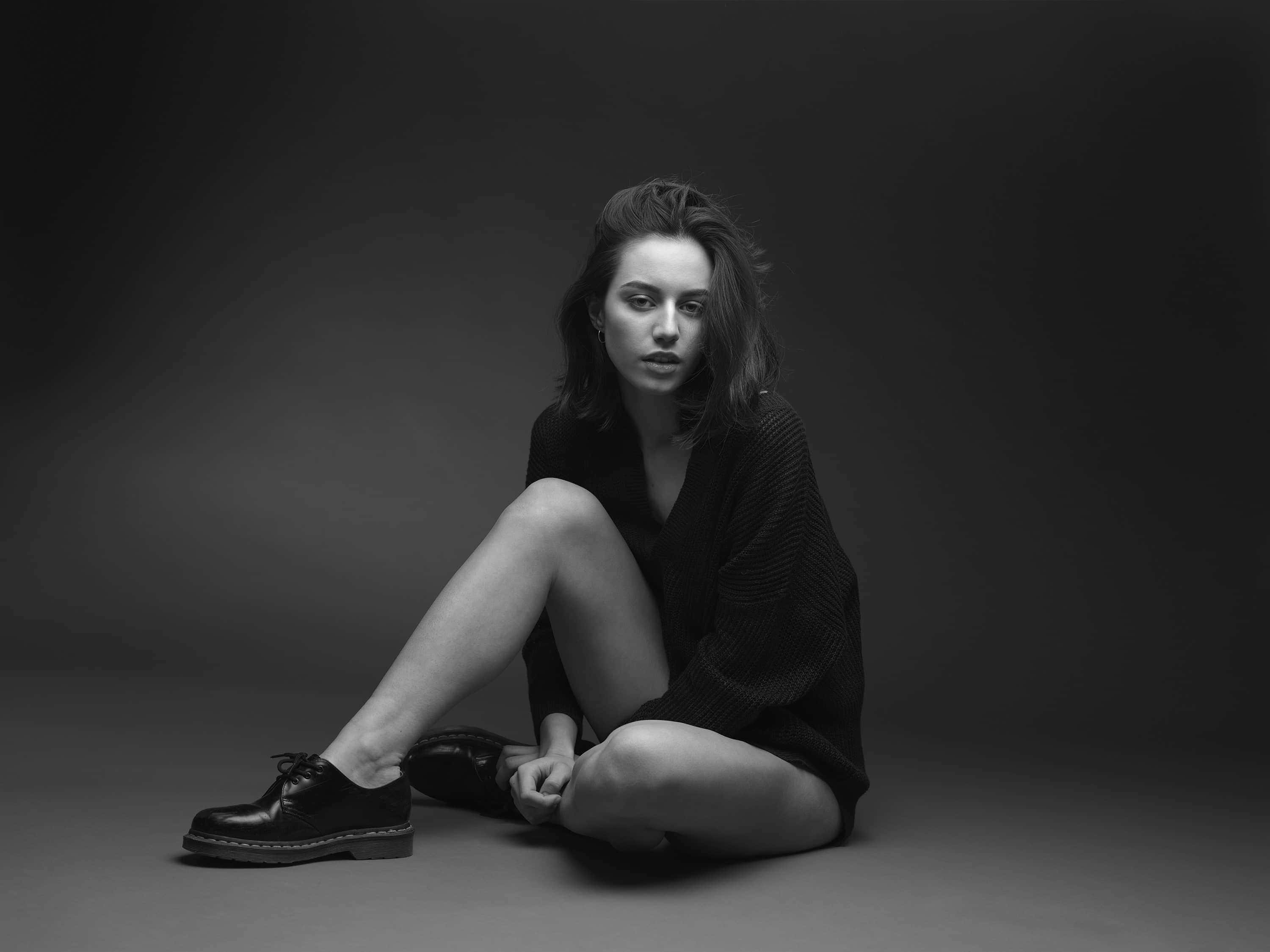 Black And White Fashion 桌布 壁紙 — 一位女士盤腿坐在深色地板上，這是一張帶有戲劇性燈光的黑白工作室肖像，氣氛憂鬱。