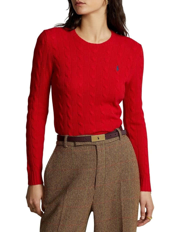 Red Sweater 桌布 壁紙 — 一位女士穿著一件鮮紅色的纜繩針織毛衣，上面有一個小小的藍色標誌，以及一條棕色的千鳥格褲，用一條金色扣環的棕色皮帶束緊。