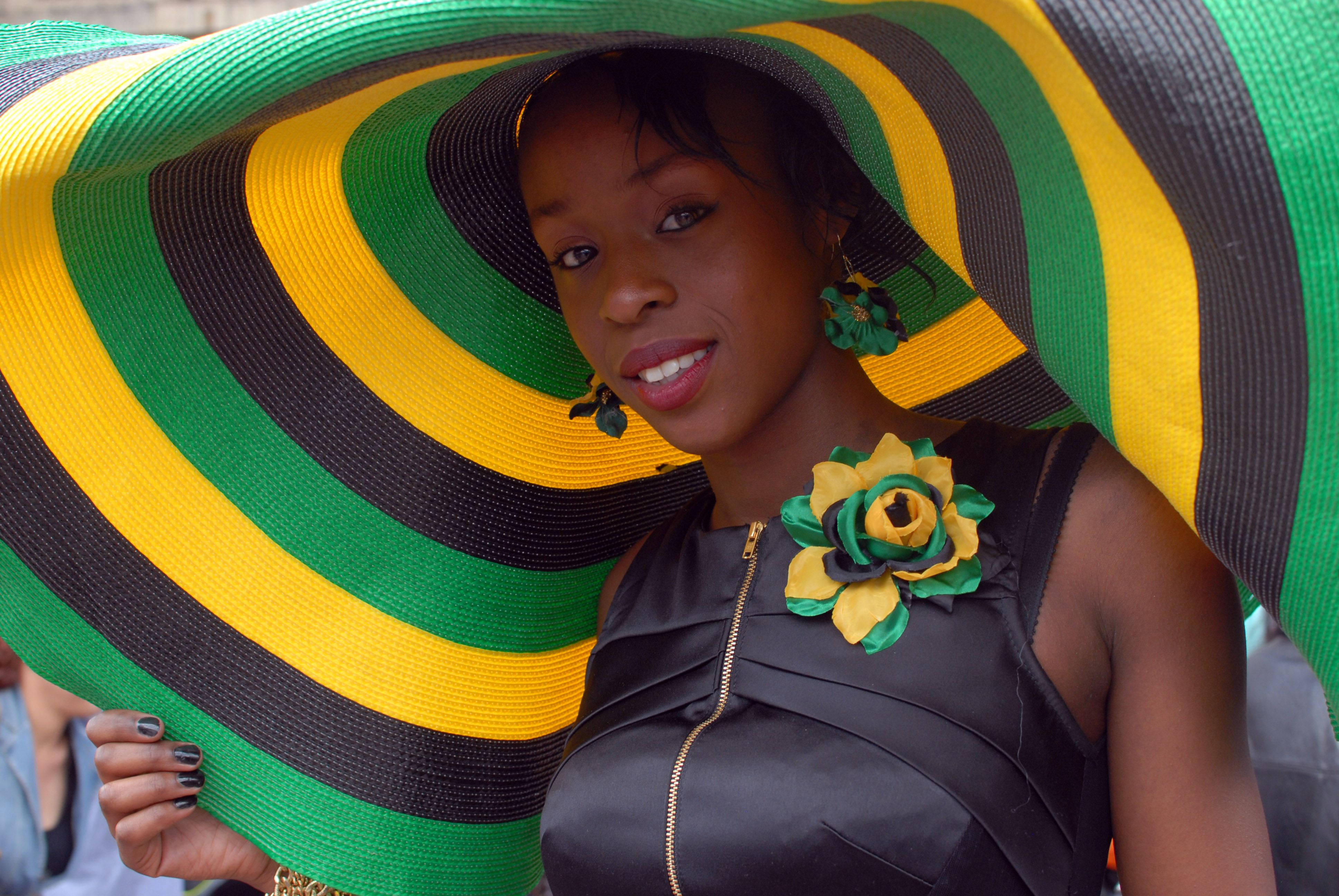 Jamaica 桌布 壁紙 — 一位女士自信地微笑，戴著一頂充滿活力的綠色、黃色和黑色條紋寬邊帽，搭配相襯的花卉飾品。