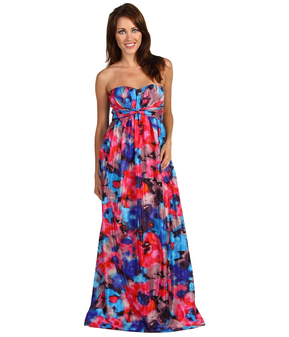 Long Dress 桌布 壁紙 — 一位女士身穿鮮豔的無肩帶長裙，裙上帶有旋轉的粉紅、藍色和紫色花卉圖案，背景為白色，她正微笑著。