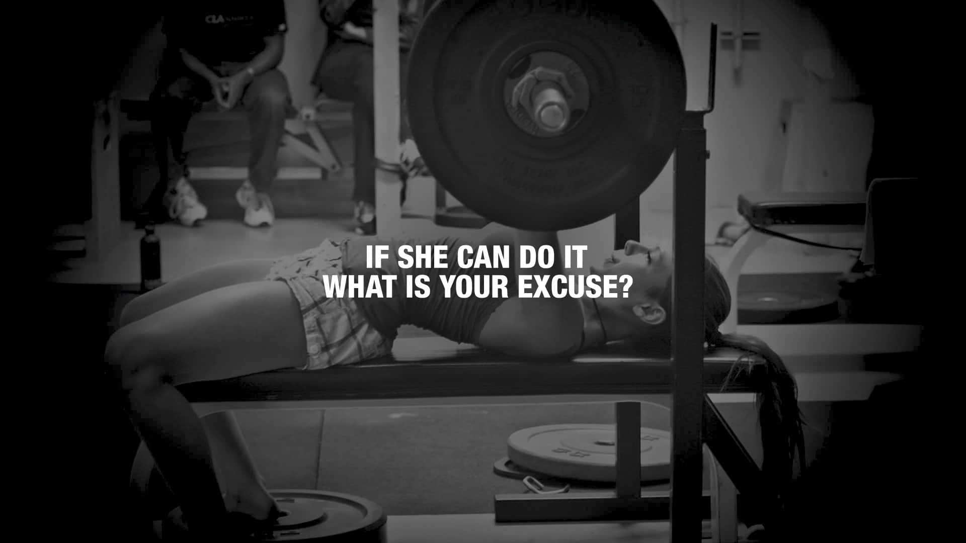Fitness 桌布 壁紙 — 一位女士躺在臥推架上，在燈光昏暗的健身房中舉起沉重的槓鈴，並疊加了勵志文字。