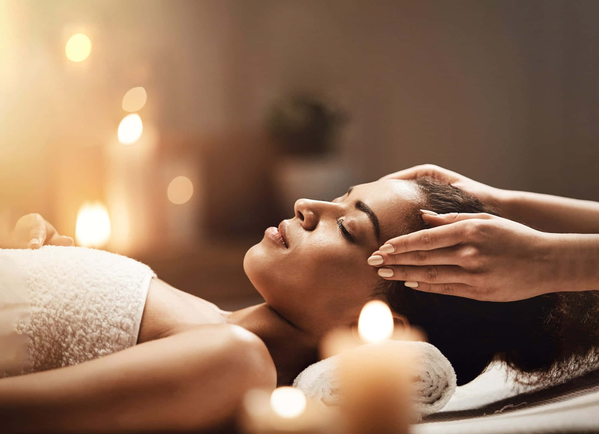 Massage 桌布 壁紙 — 一位女士閉上眼睛放鬆，雙手輕柔地按摩她的額頭，周圍是發光的蠟燭，營造出寧靜的水療環境。