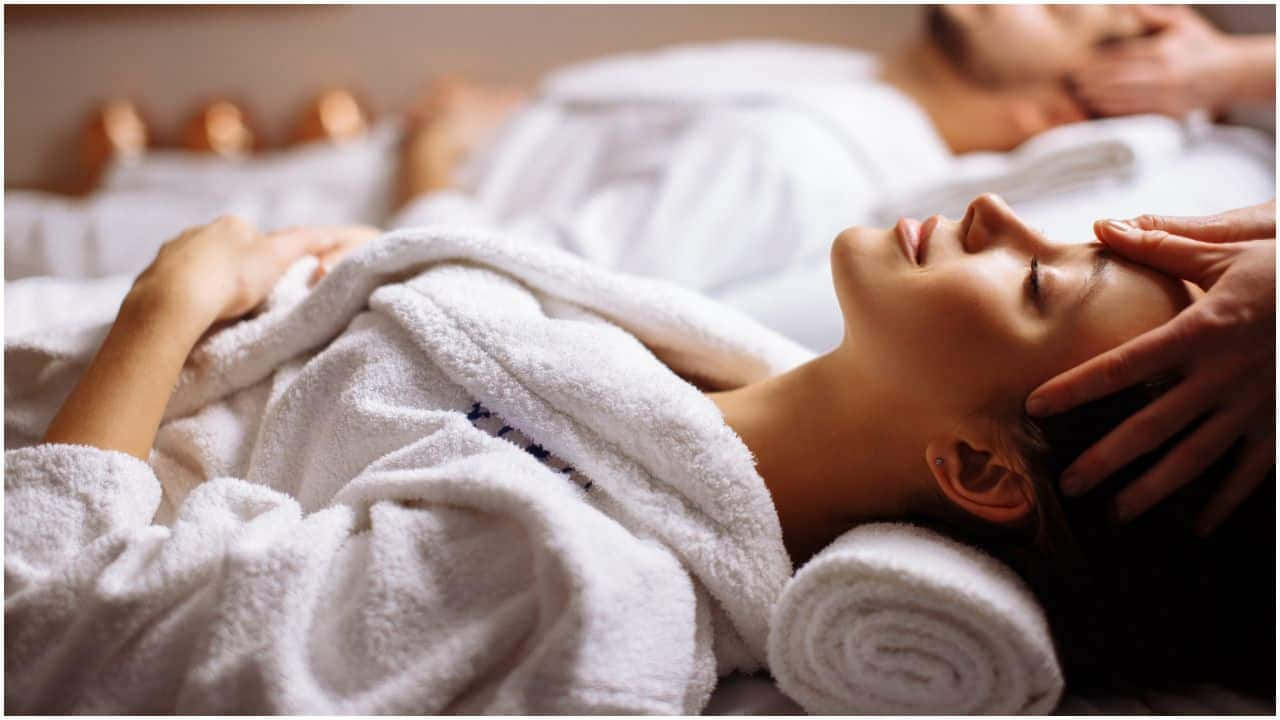 Massage 桌布 壁紙 — 一位女士閉上眼睛放鬆，雙手輕輕按摩她包裹在柔軟白色毛巾中的額頭。