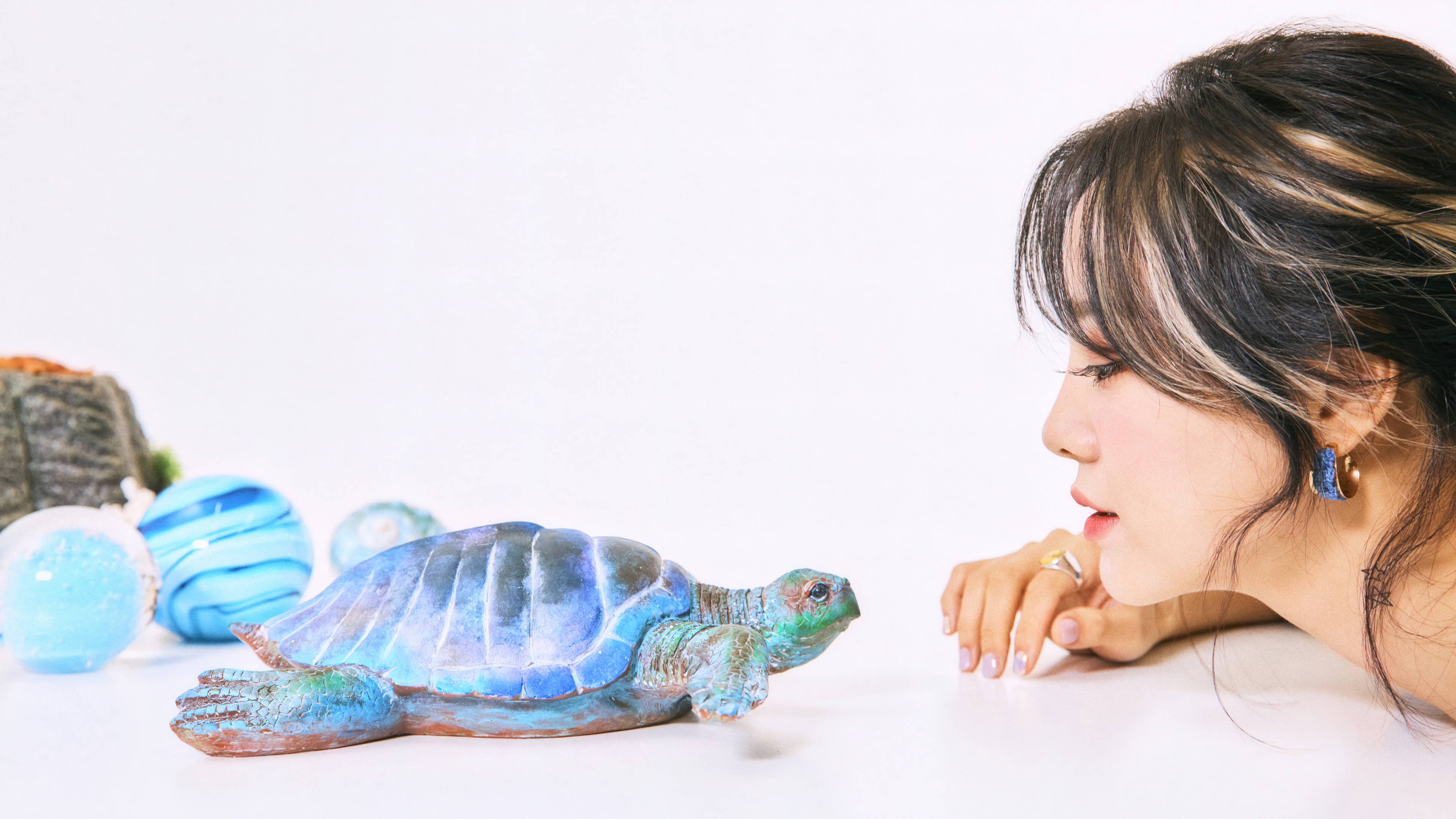 桌布 壁紙 — 一位女士靠近凝視白色表面上的一個藍綠色烏龜雕像，附近有裝飾球體。