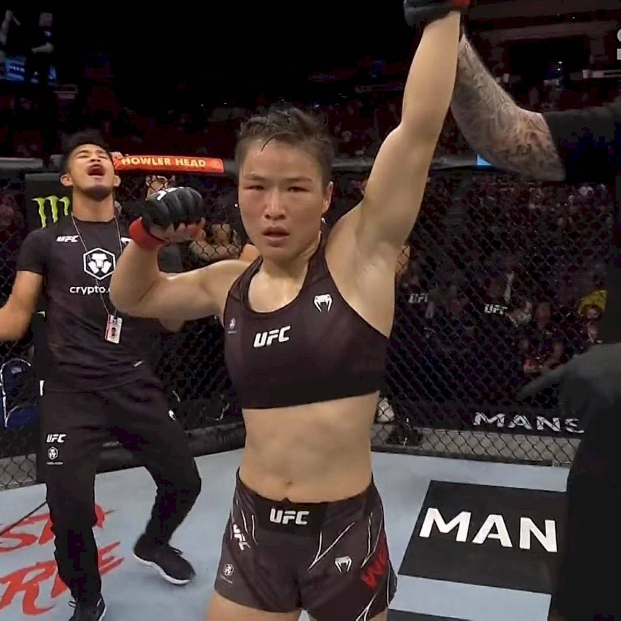 Champion 桌布 壁紙 — 一位女性MMA拳手在UFC八角籠中舉起手臂慶祝勝利，她的教練在身後歡呼。