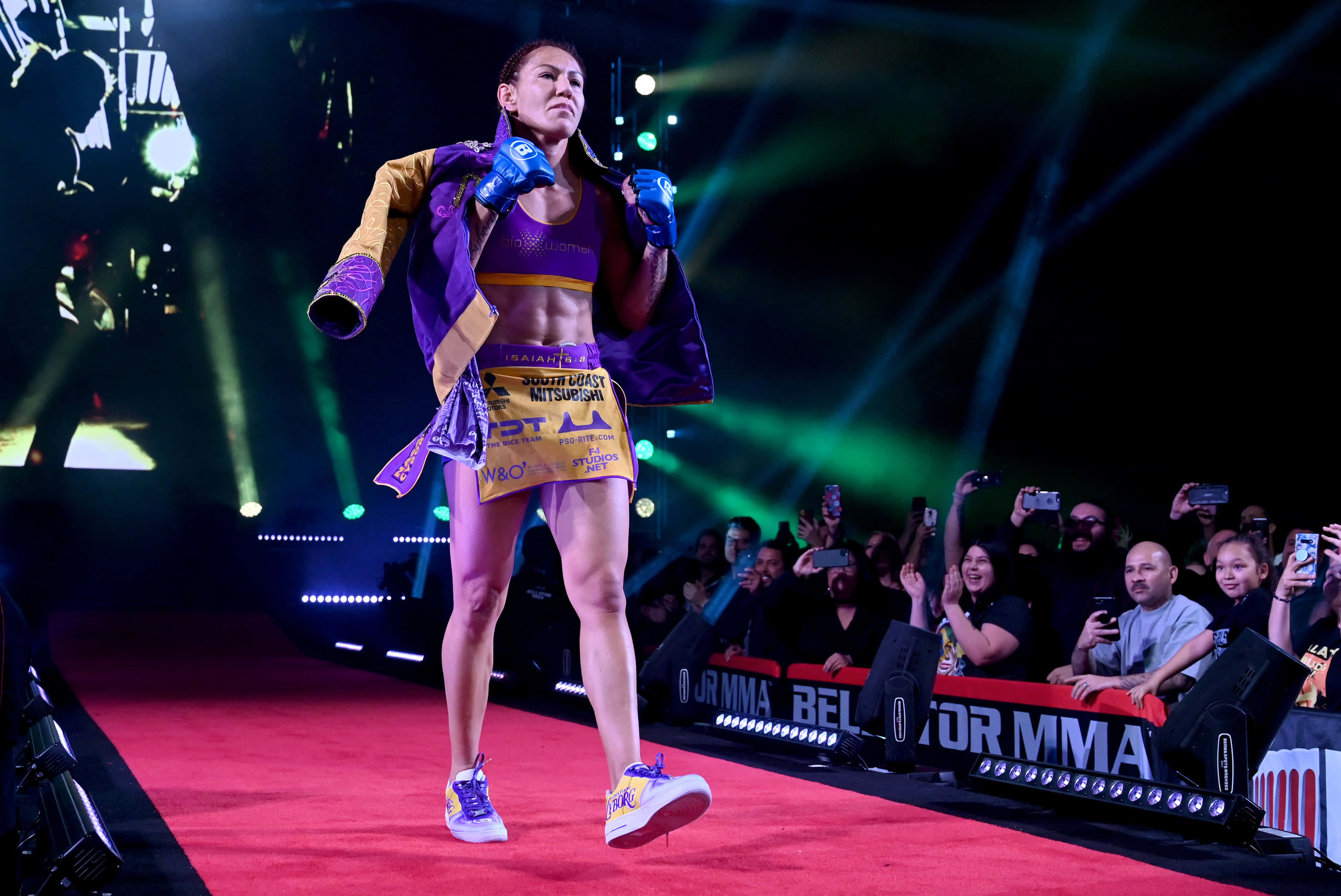 UFC 桌布 壁紙 — 一位女性MMA拳手在充滿活力的綠色舞台燈光下自信地走過紅地毯，身後是熱情的群眾。