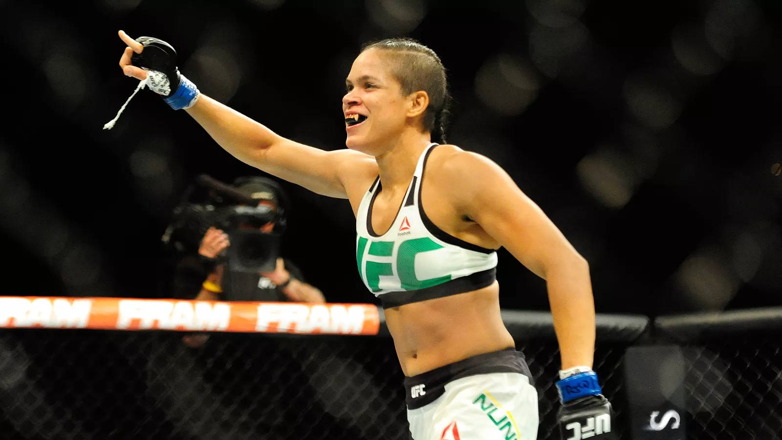MMA 桌布 壁紙 — 一位女性MMA拳手在八角籠中慶祝勝利，高舉拳頭，表情喜悅。
