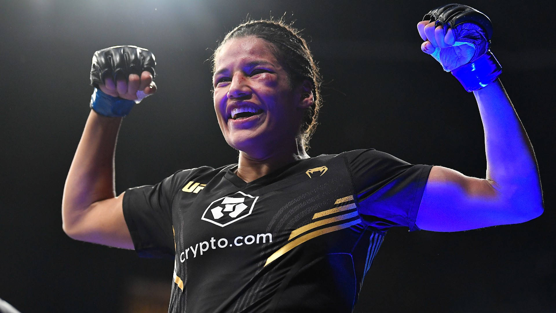 MMA 桌布 壁紙 — 一位女性MMA拳手在戲劇性的藍色競技場燈光下舉起拳頭慶祝勝利。
