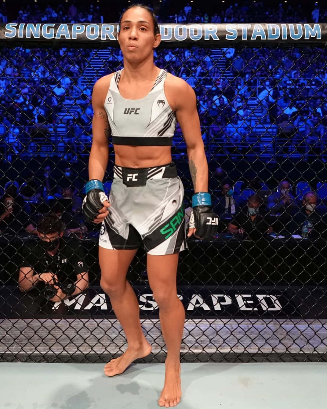 UFC 桌布 壁紙 — 一位女性MMA拳手自信地赤腳站在新加坡室內體育館的八角籠內，場館燈光明亮。