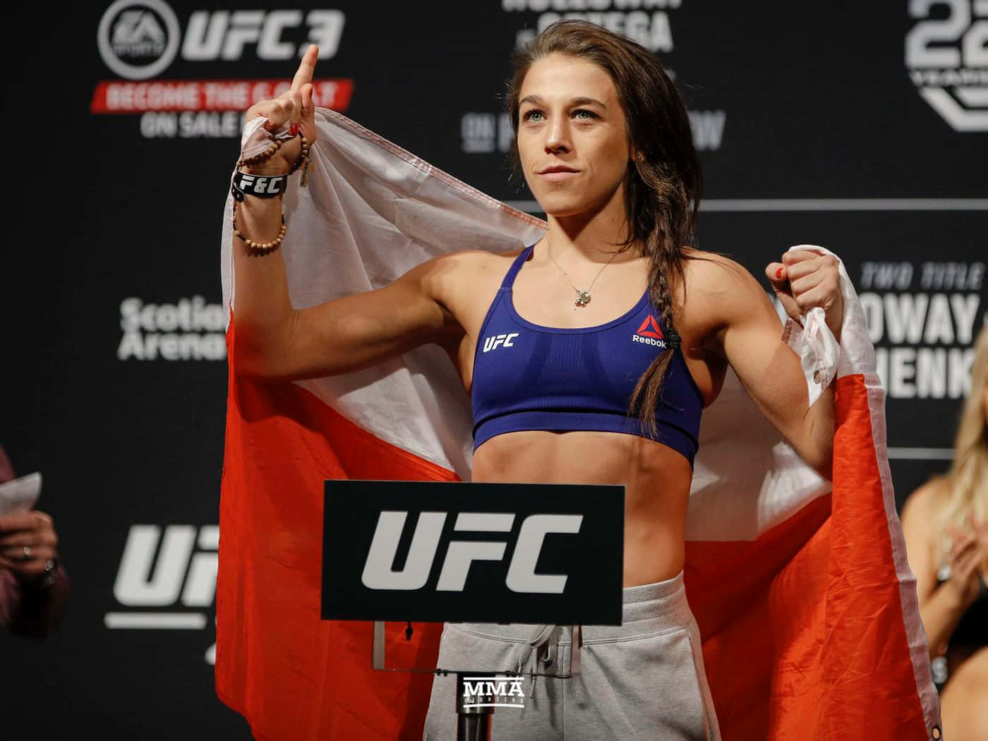 professional 桌布 壁紙 — 一位女性UFC拳手在稱重活動中自信地站在體重計上，手持波蘭國旗。