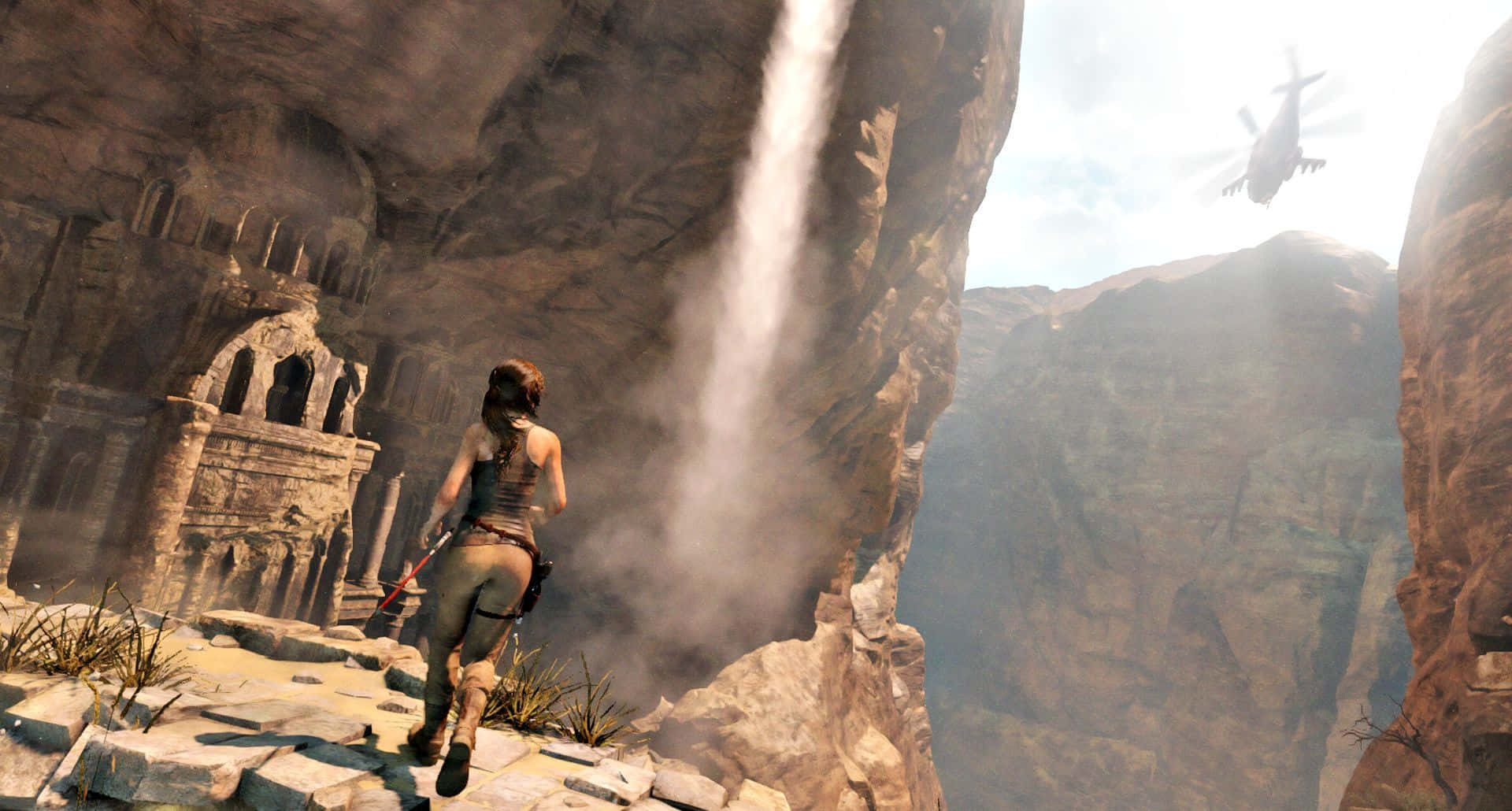 Lara Croft 桌布 壁紙 — 一位女性冒險家跑過峽谷中瀑布旁的石頭廢墟，一架直升機在頭頂飛過。