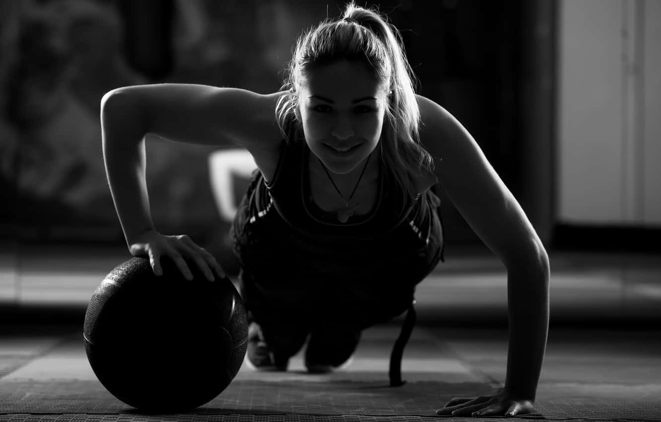 Exercise 桌布 壁紙 — 一位女性在健身房微笑，同時以平板支撐姿勢拿著藥球，黑白照片。