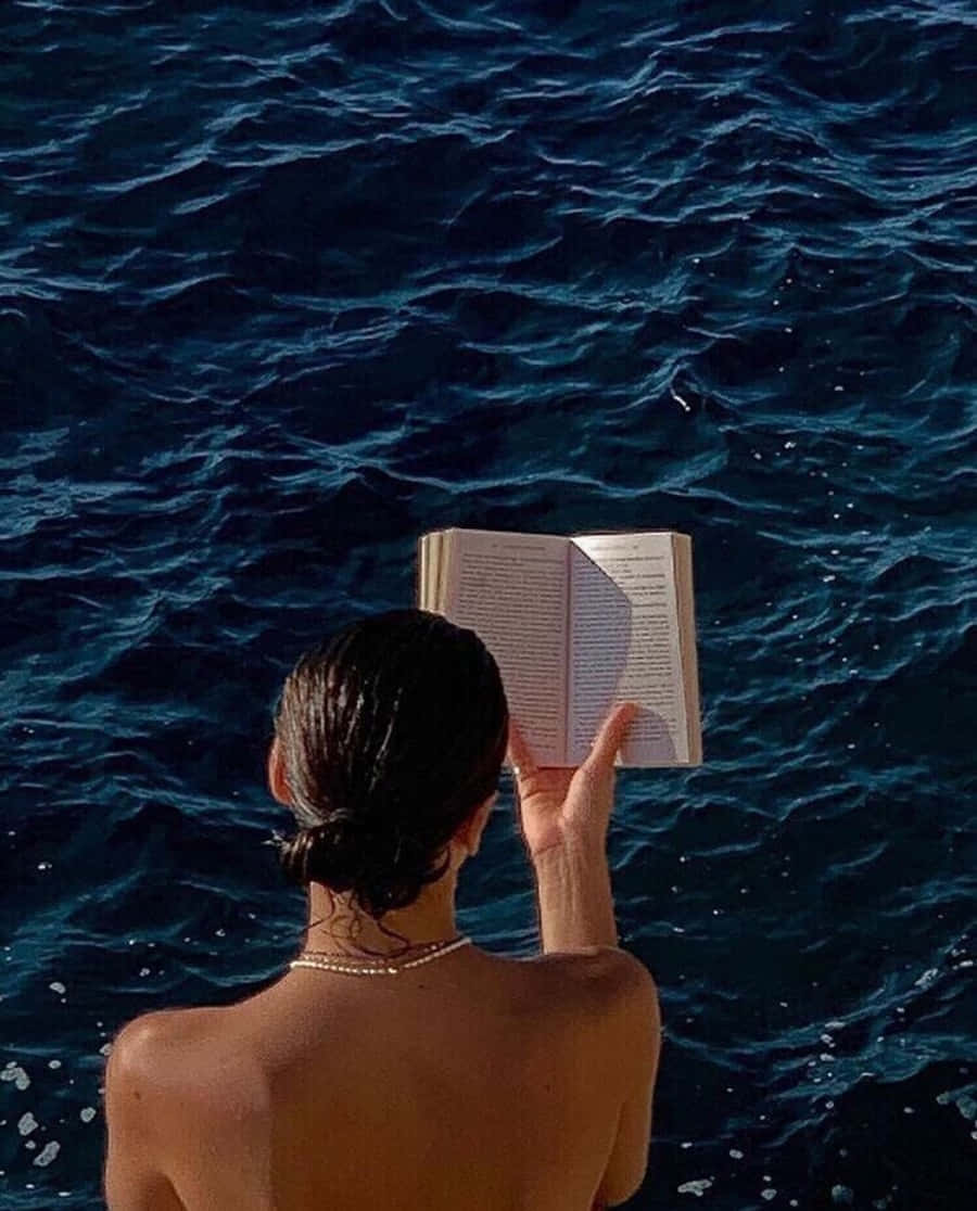 一位女性在海洋中的船上閱讀書籍 壁紙