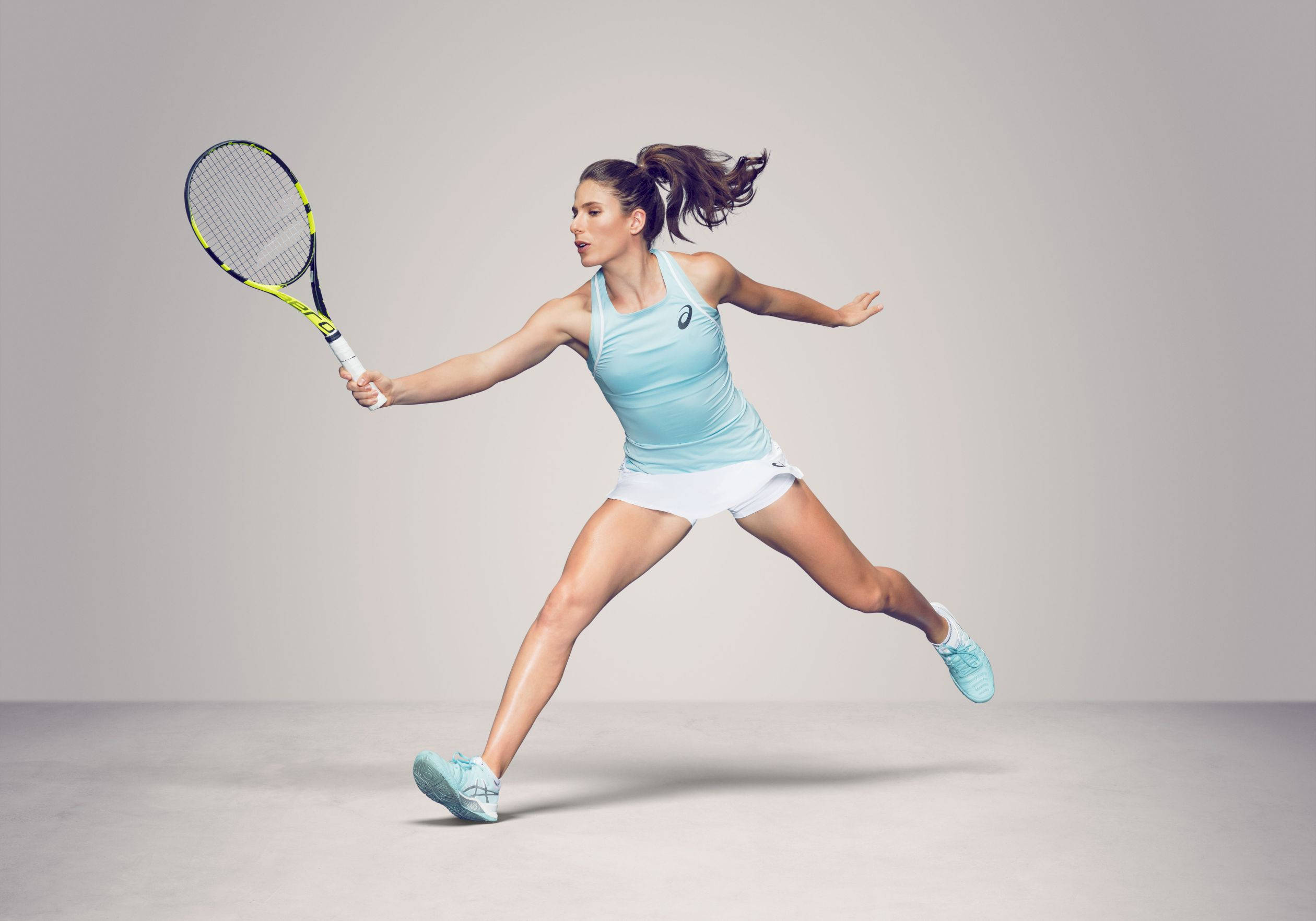 Athletic 桌布 壁紙 — 一位女性網球選手在純色攝影棚背景前揮拍中，穿著淺藍色運動裝備。