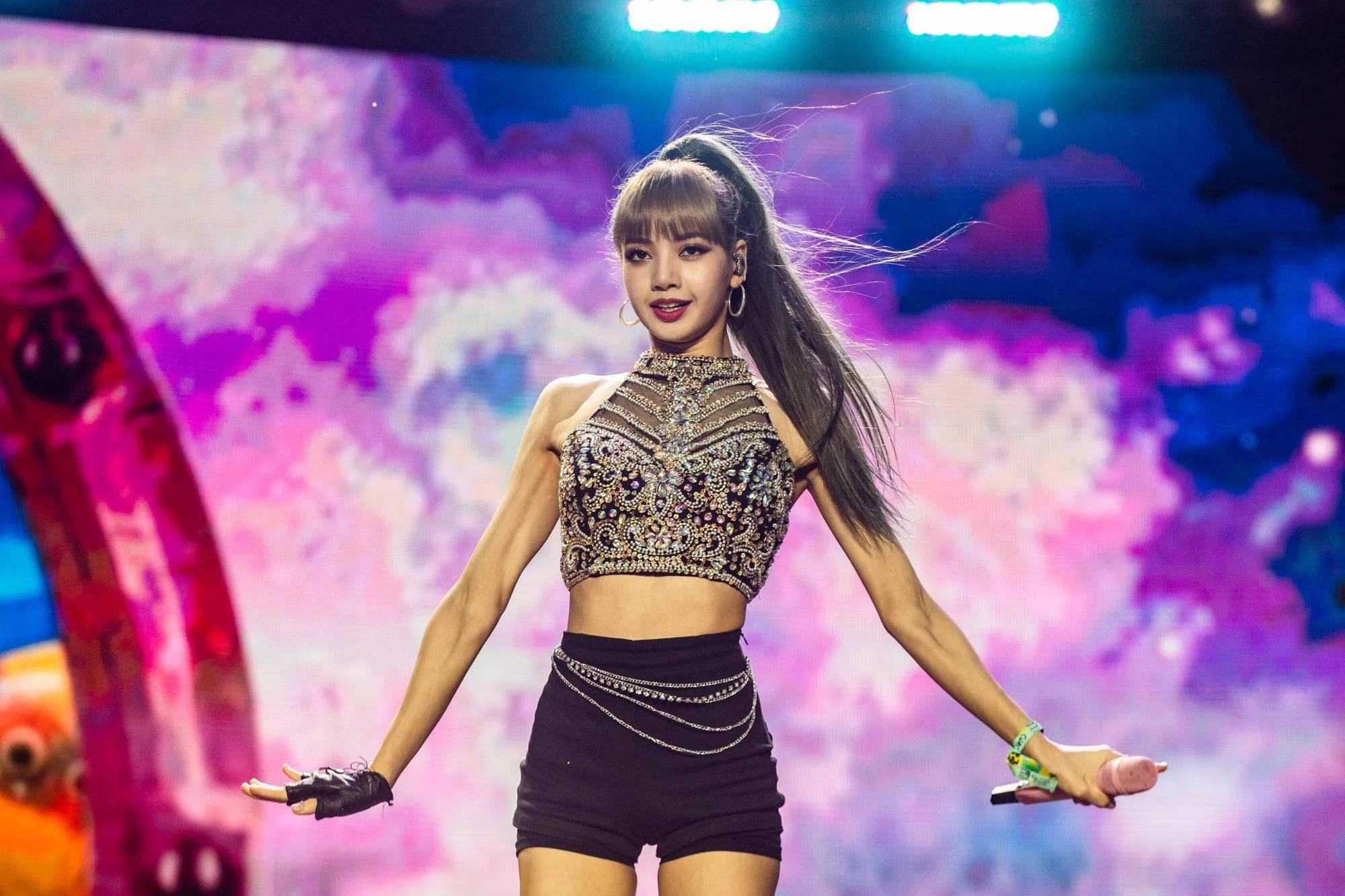 Lalisa 桌布 壁紙 — 一位女性表演者穿著閃閃發光的露臍上衣和黑色短褲，在充滿活力的紫色和藍色舞台上，伴隨著動態燈光，充滿活力地跳舞。