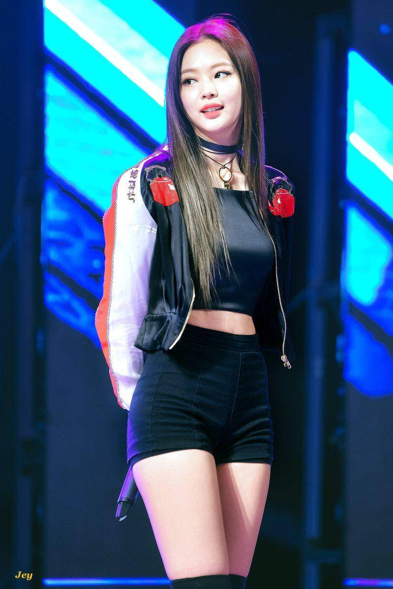 Jennie 桌布 壁紙 — 一位女性表演者身穿黑色露臍上衣和短褲，搭配白色和紅色外套，自信地站在被鮮豔藍色燈光照亮的舞台上。