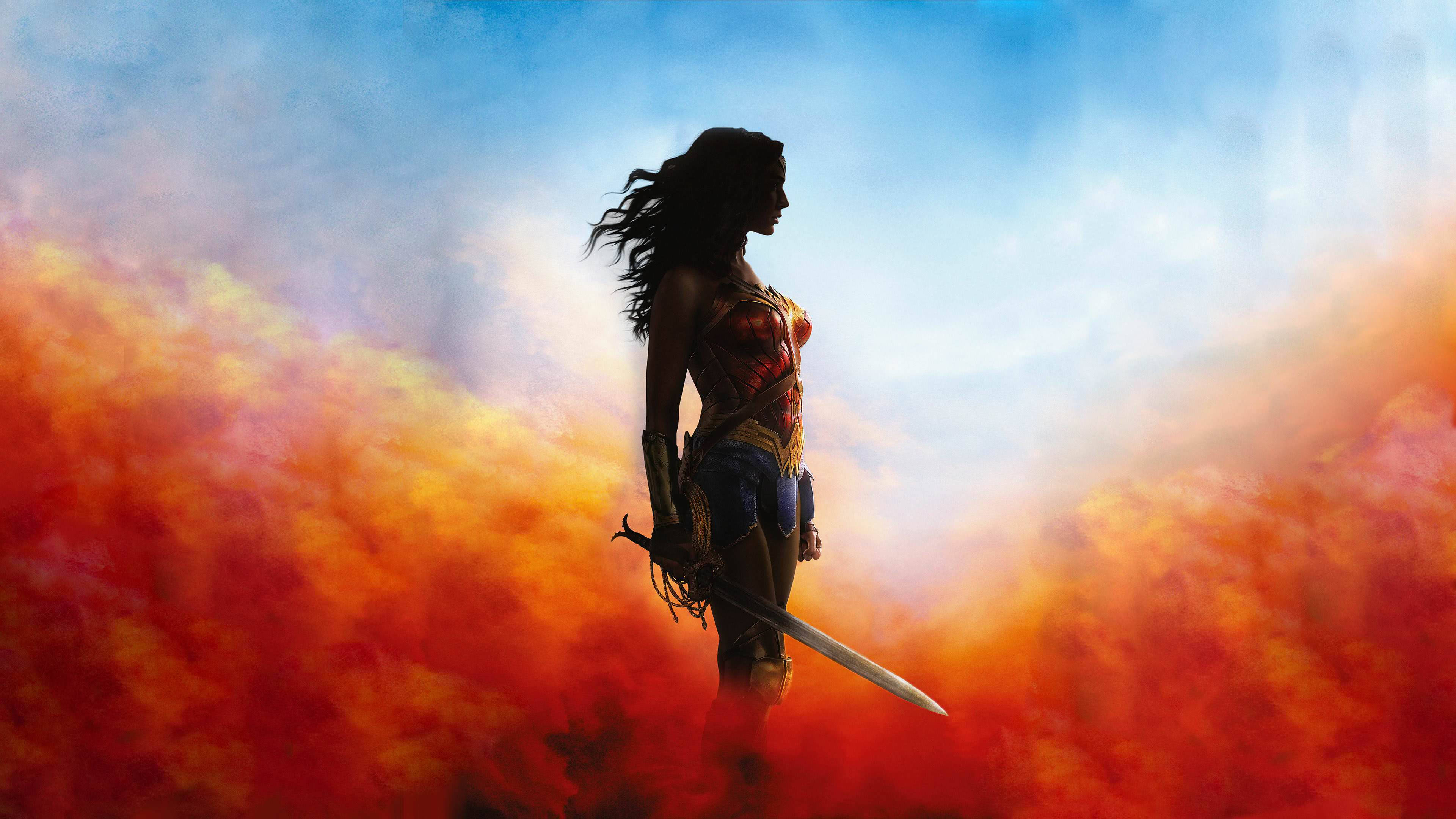 Wonder Woman 桌布 壁紙 — 一位女戰士手持劍，在熾熱的橙色和藍色天空下以剪影站立。