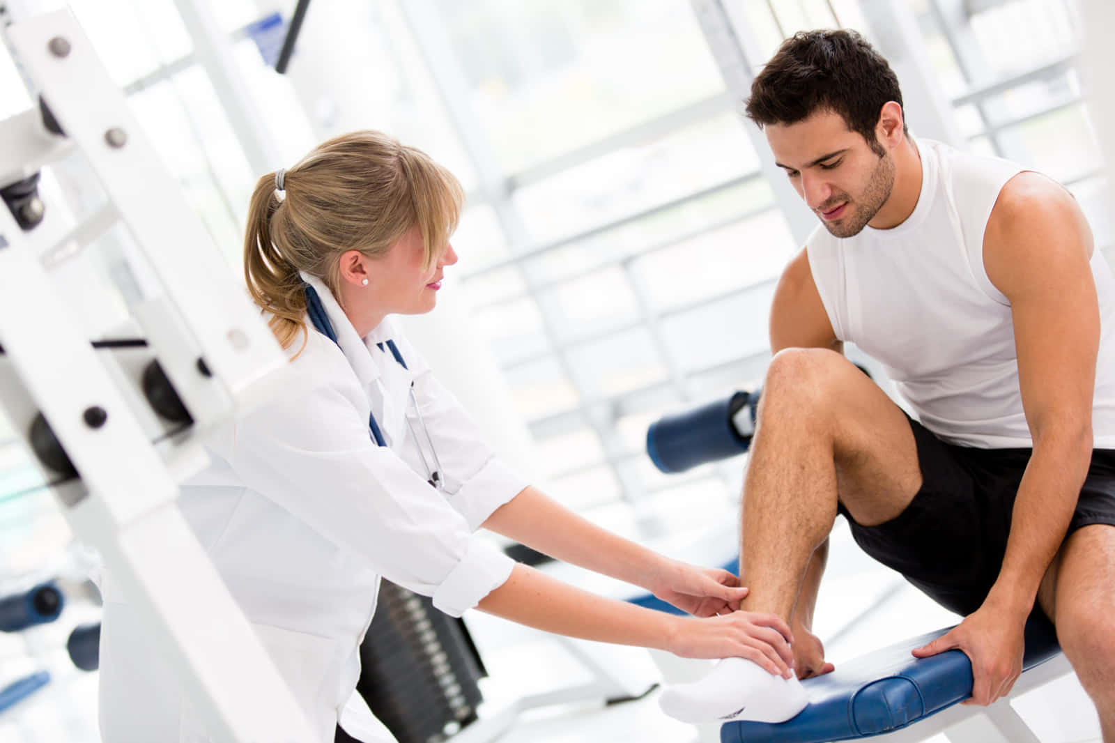 Exercise 桌布 壁紙 — 一位女物理治療師在明亮現代的健身房用運動器材檢查一位男士的腳踝。