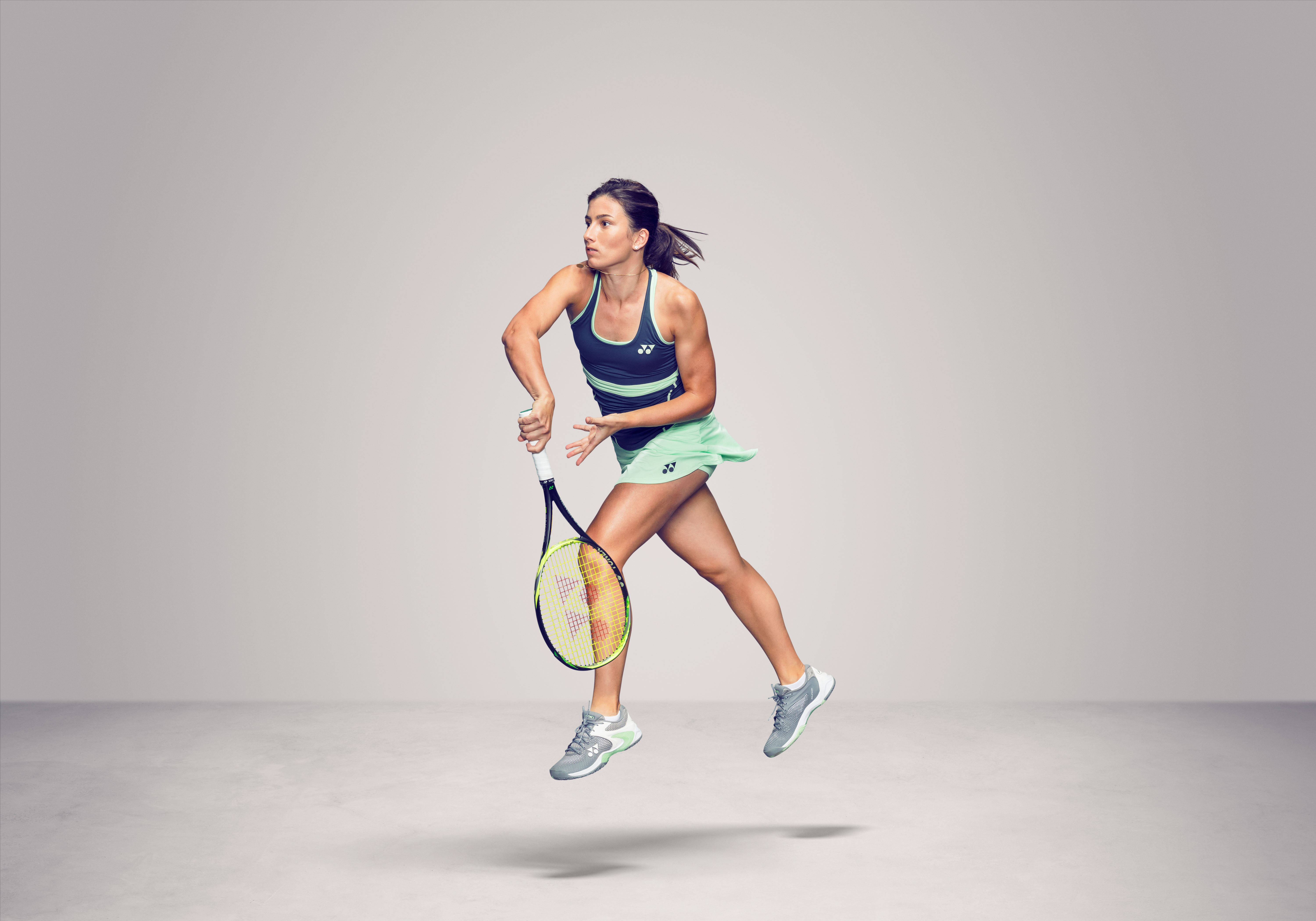 Tennis 桌布 壁紙 — 一位女網球運動員在半空中，在極簡風格的攝影棚背景下執行強力的正手揮拍。
