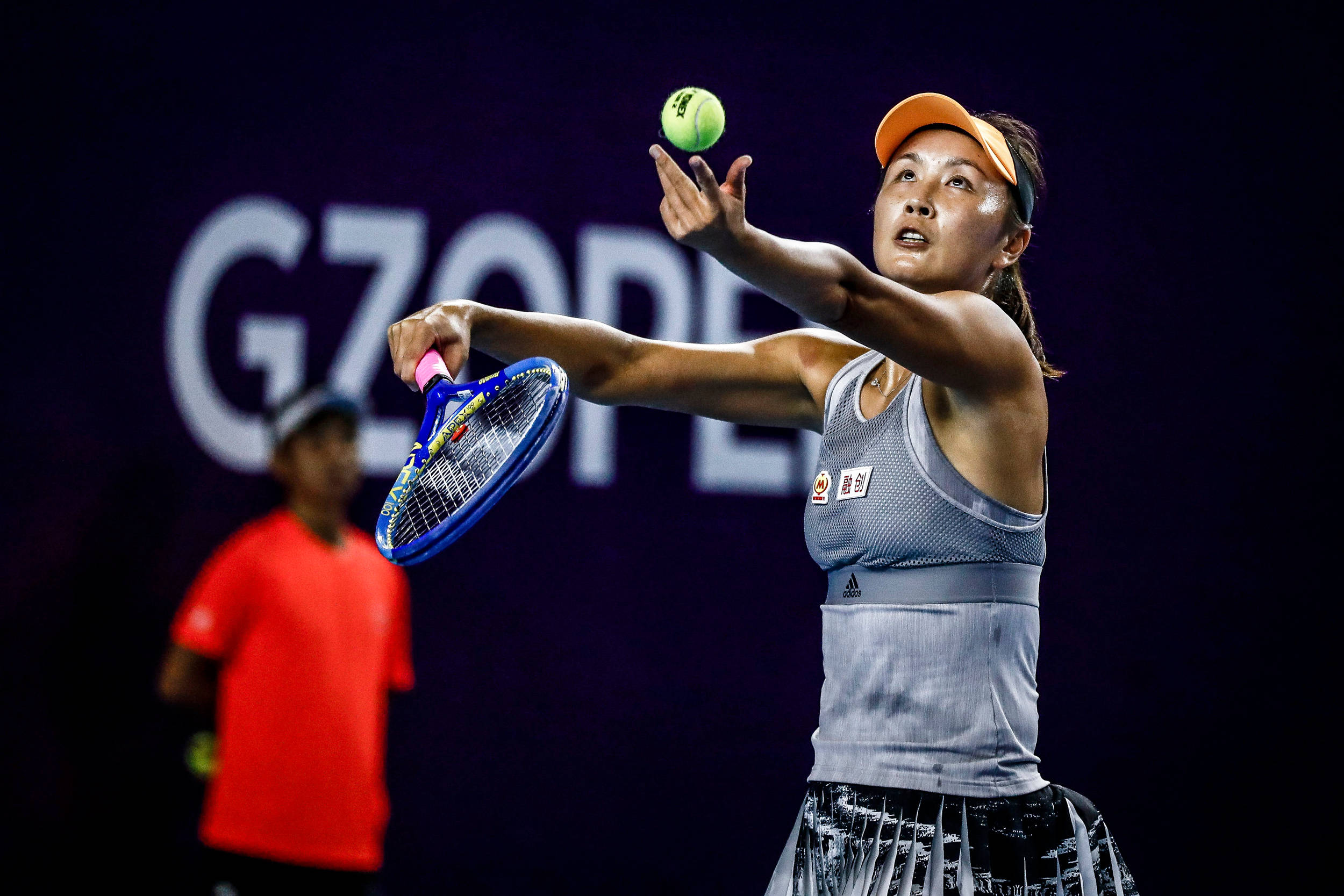 運動 桌布 壁紙 — 一位女網球運動員在帶有 'GZOPEN' 標牌的黑暗背景下專注發球。