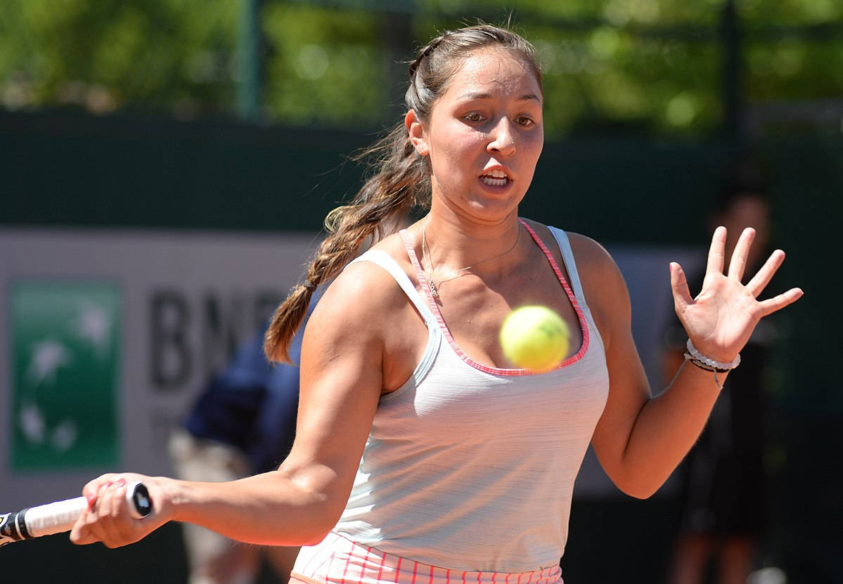 Tennis 桌布 壁紙 — 一位女網球運動員在揮拍中途，在陽光普照的紅土場上專注地擊打黃色網球。