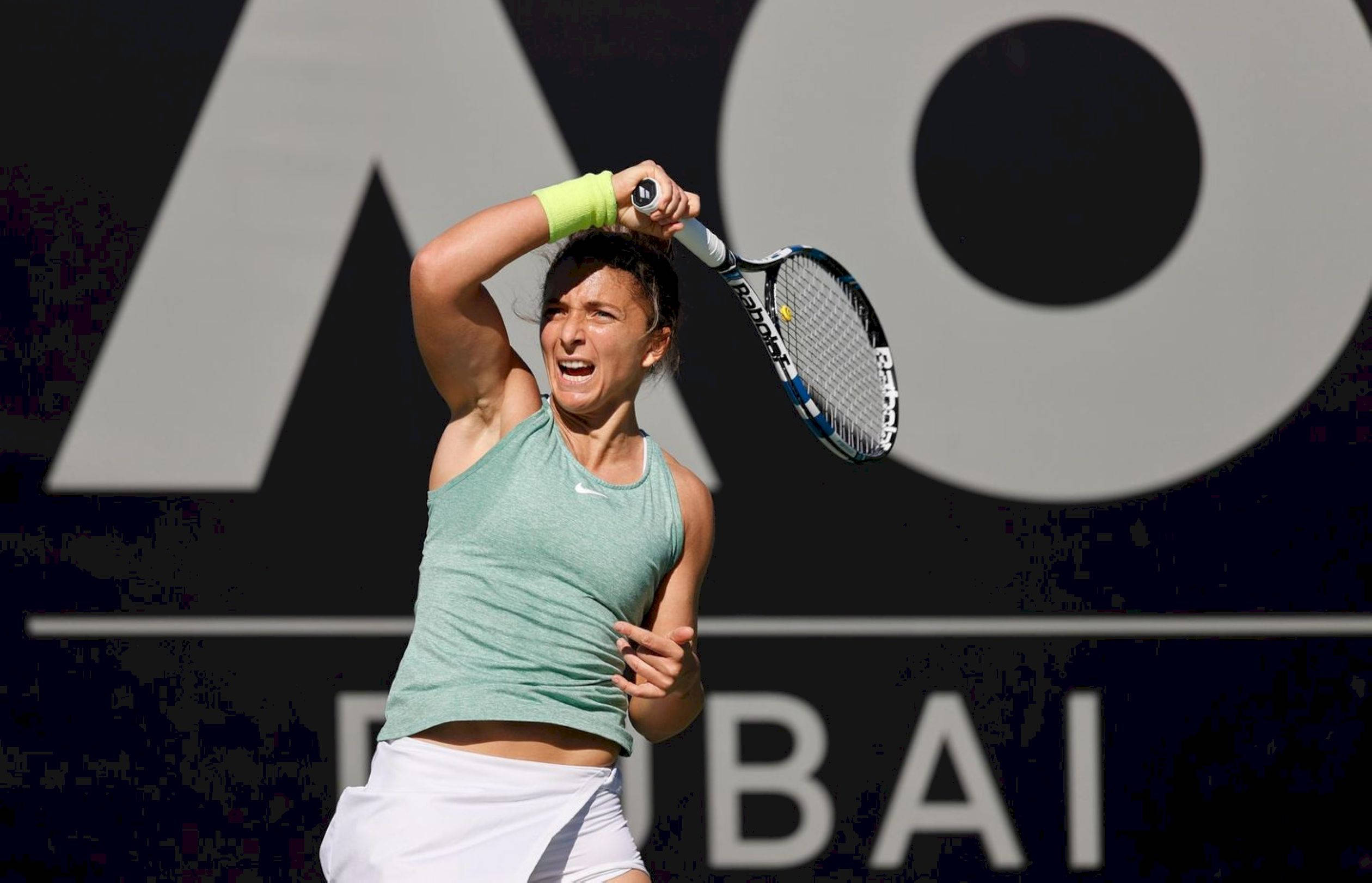 Athletic 桌布 壁紙 — 一位女網球運動員在深色背景前專注揮拍，背景有大型AO Dubai品牌標誌。