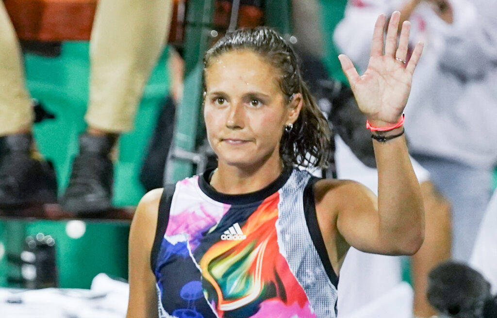 Athletic 桌布 壁紙 — 一位女網球運動員在球場上穿著鮮豔多彩的運動上衣向球迷揮手。
