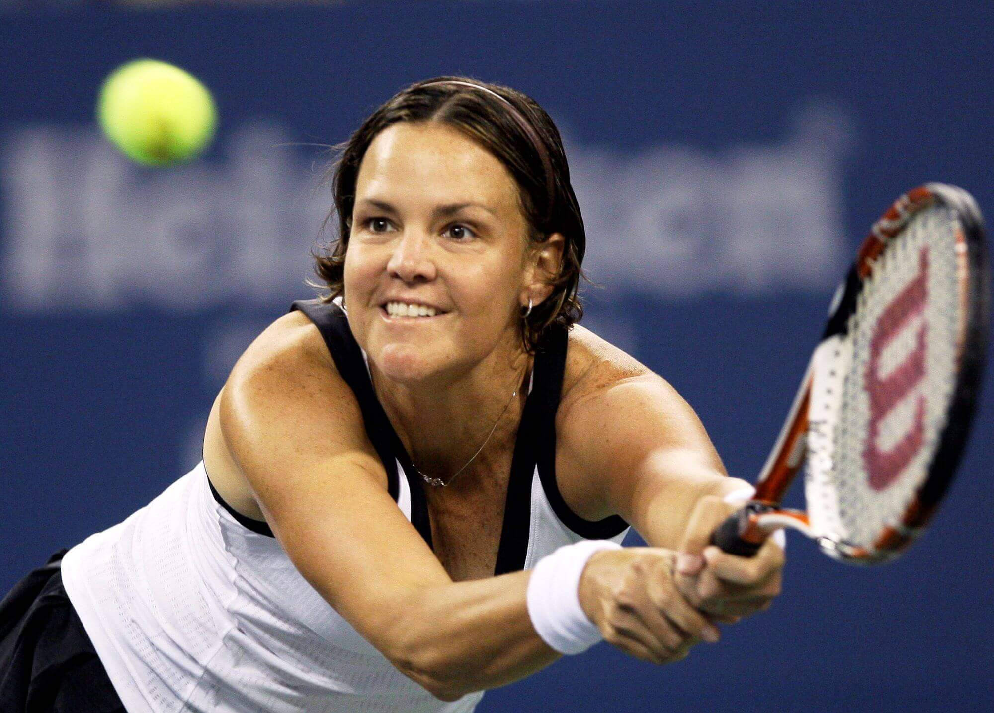 Tennis 桌布 壁紙 — 一位女網球運動員在藍色球場背景下，揮拍擊向明亮的黃色網球，露出專注的笑容。
