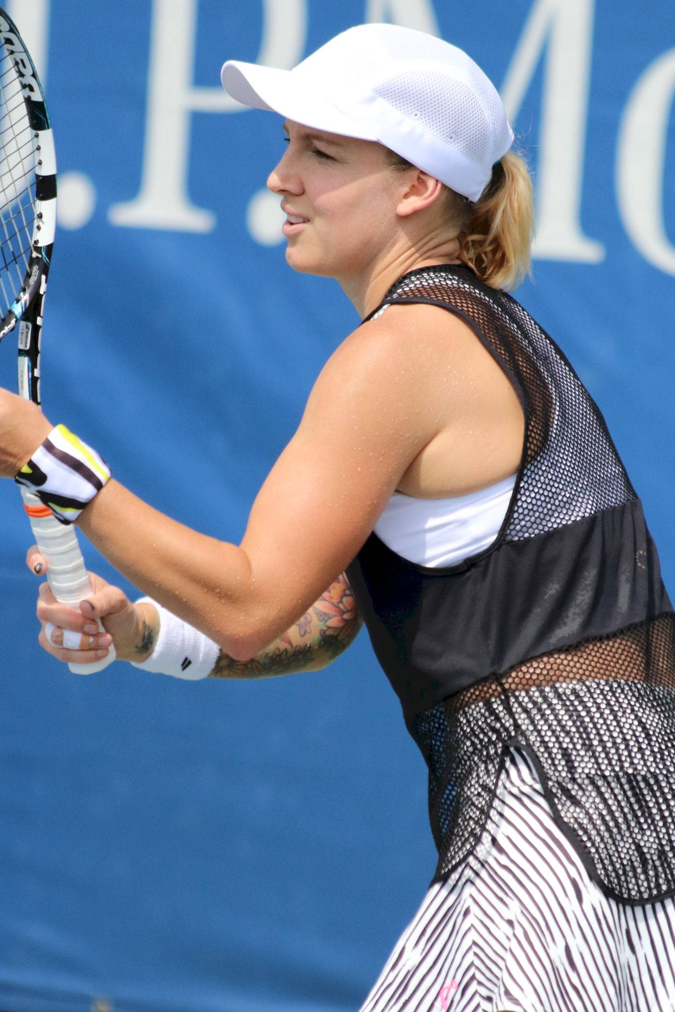 Tennis 桌布 壁紙 — 一位女網球運動員正在揮拍，戴著白色帽子，穿著黑色網狀服裝，背景是藍色球場。