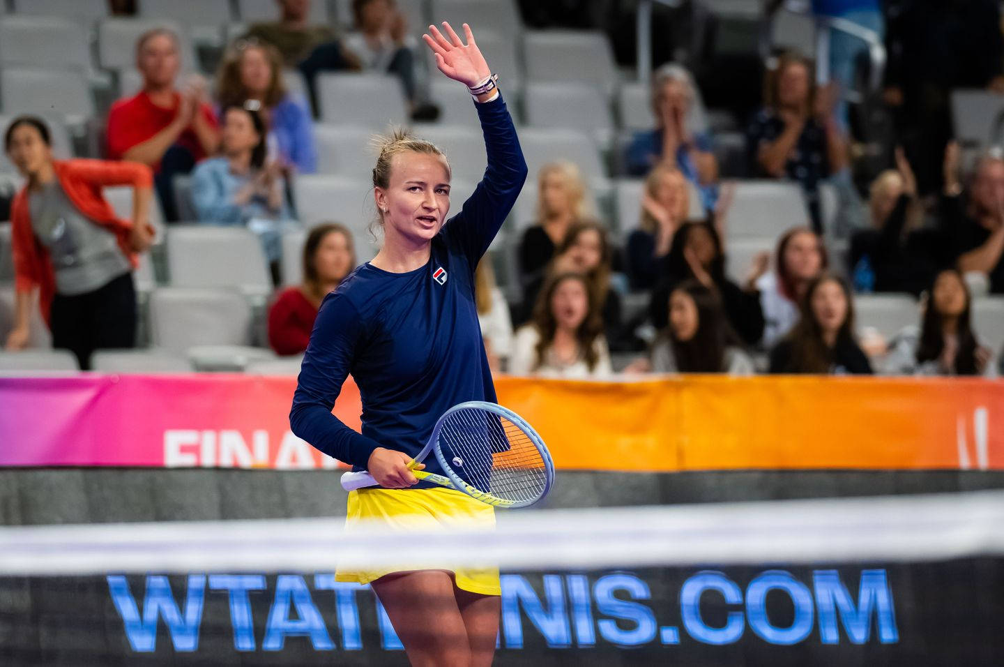 Woman 桌布 壁紙 — 一位女網球選手在帶有 'WTATENNIS.COM' 標誌的球場上，手持球拍向歡呼的球迷揮手。