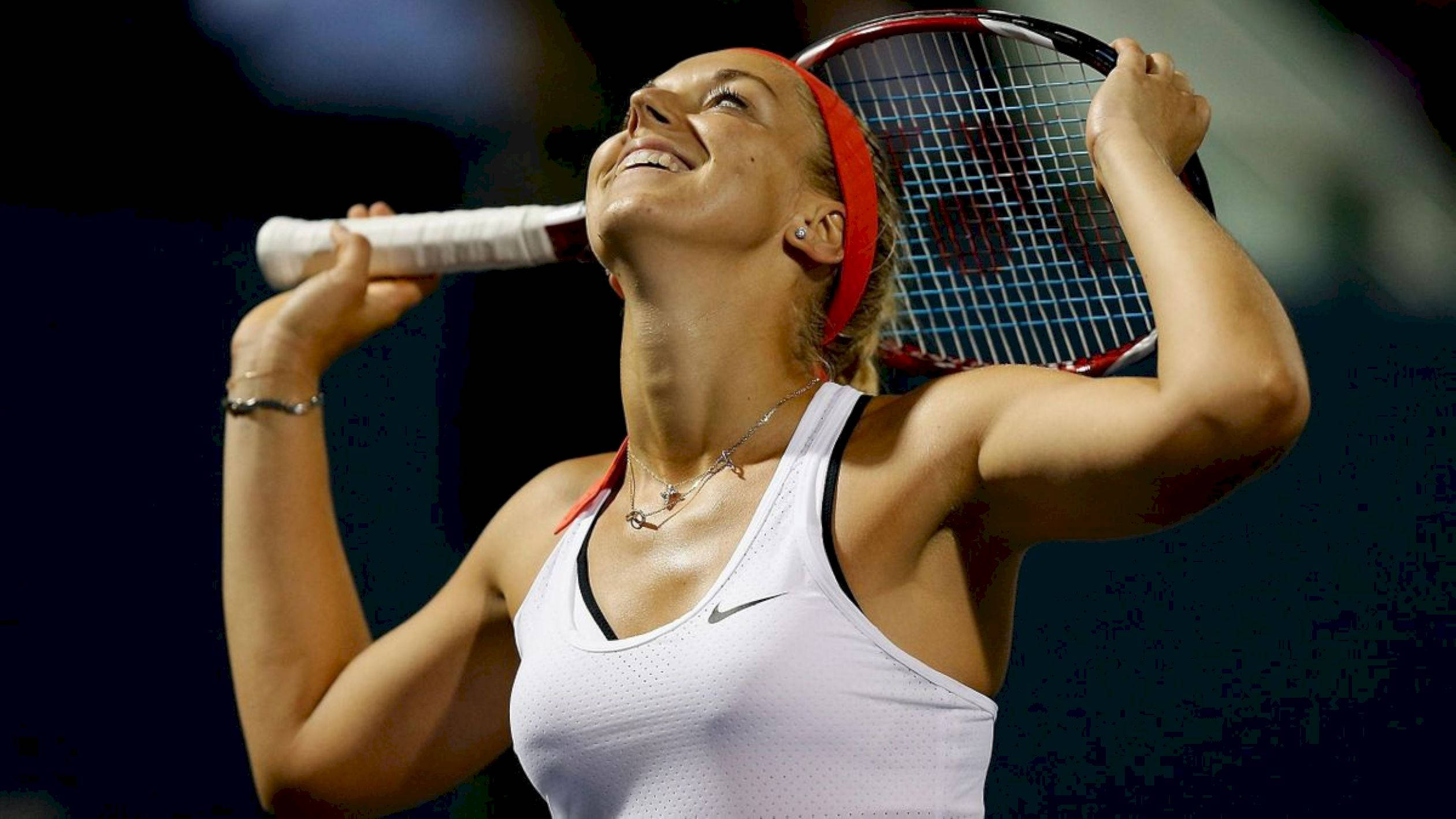 Tennis 桌布 壁紙 — 一位女網球選手在明亮的體育場燈光下比賽時，得意地微笑著將球拍高舉過頭。
