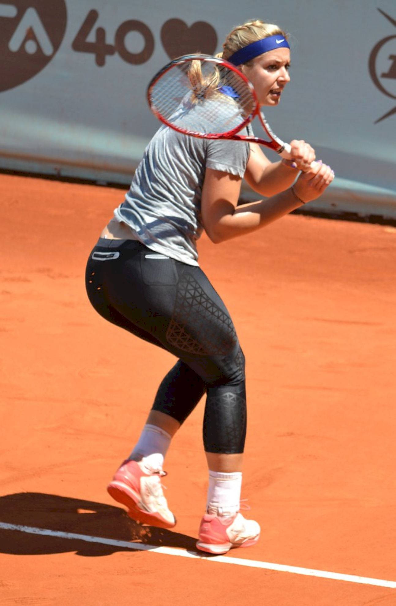 Tennis 桌布 壁紙 — 一位女網球選手在陽光普照的紅土球場上揮拍，專注力極強，姿態充滿運動感。