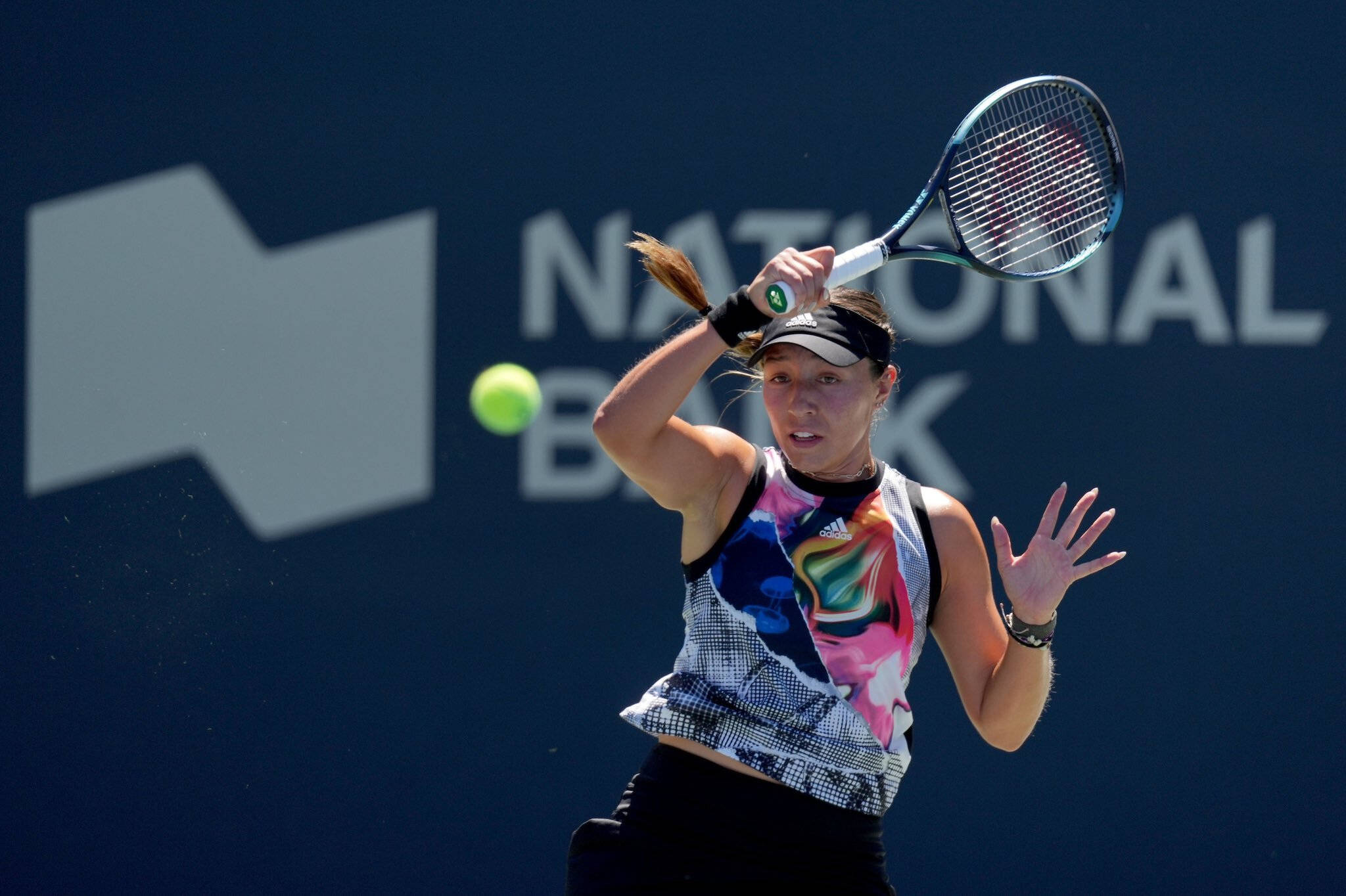 Tennis 桌布 壁紙 — 一位女網球選手揮動球拍，將一個亮黃色的球擊向帶有白色品牌標誌的深藍色牆壁。
