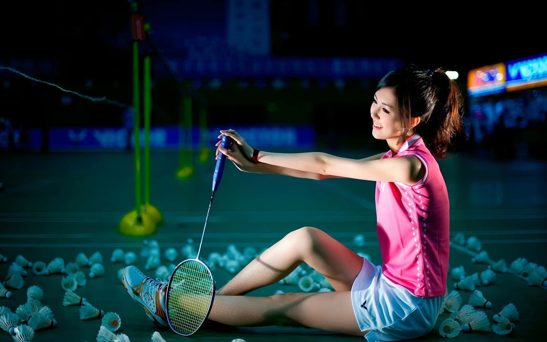 Best Badminton 桌布 壁紙 — 一位女羽毛球運動員在晚上坐在球場上，被羽毛球包圍，手持球拍，表情平靜。