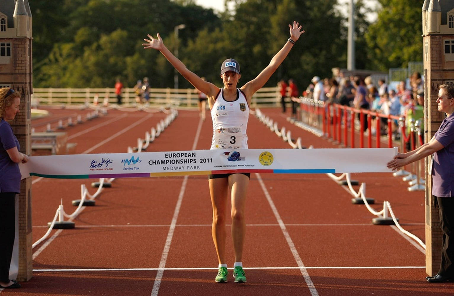 運動 桌布 壁紙 — 一位女運動員在2011年歐洲錦標賽上，在紅色跑道上高舉雙臂衝過終點線，展現勝利姿態。