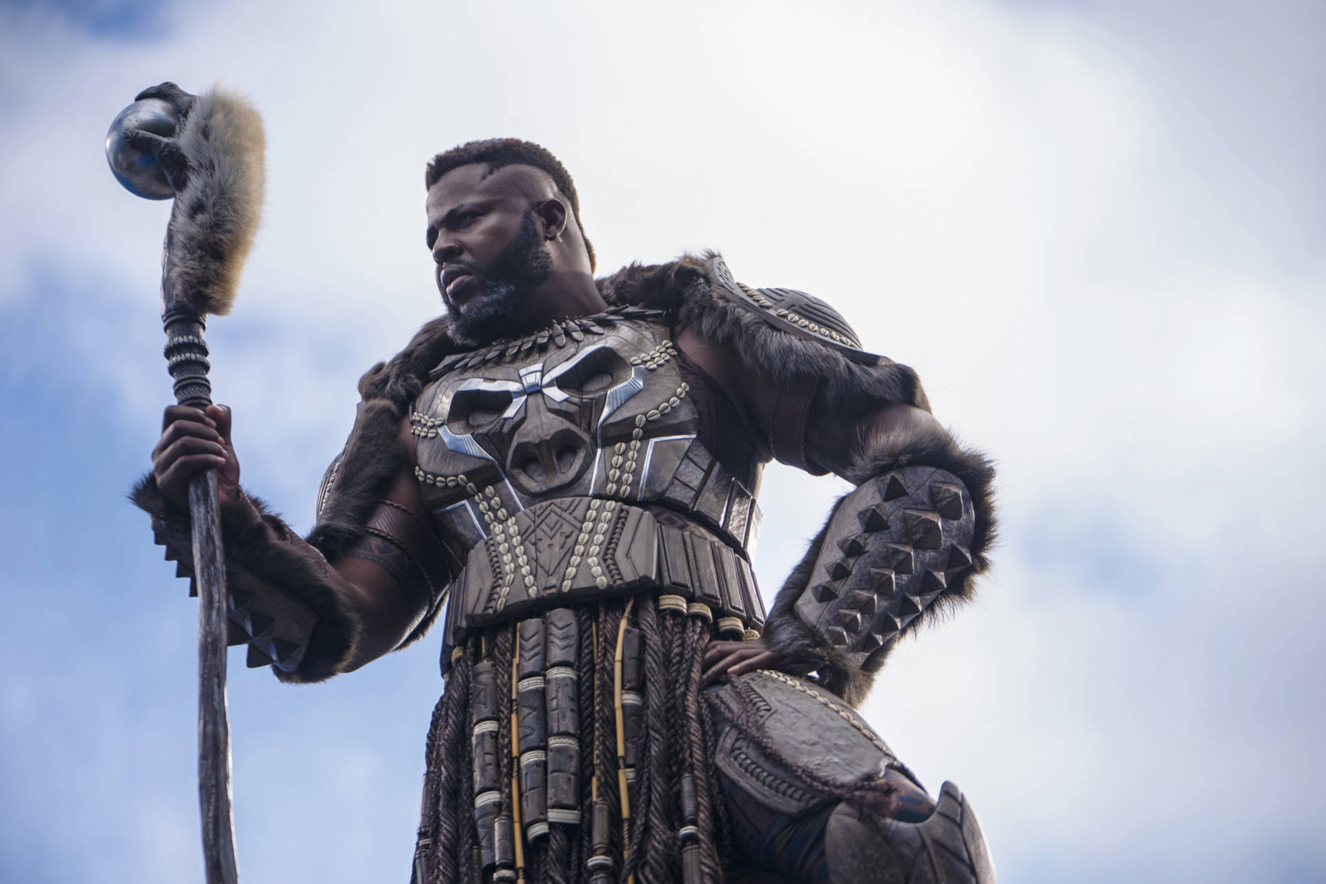 Wakanda 桌布 壁紙 — 一位威嚴的戰士身穿精緻的部落盔甲，在陰雲密佈的天空下手持儀式權杖。