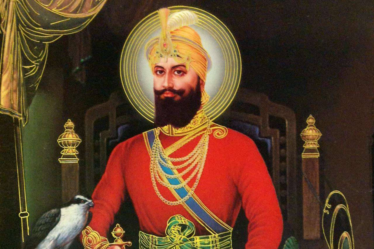Guru Gobind Singh Ji 桌布 壁紙 — 一位威嚴的錫克教戰士身穿紅袍和金色頭巾，坐在王座上，旁邊棲著一隻獵鷹。