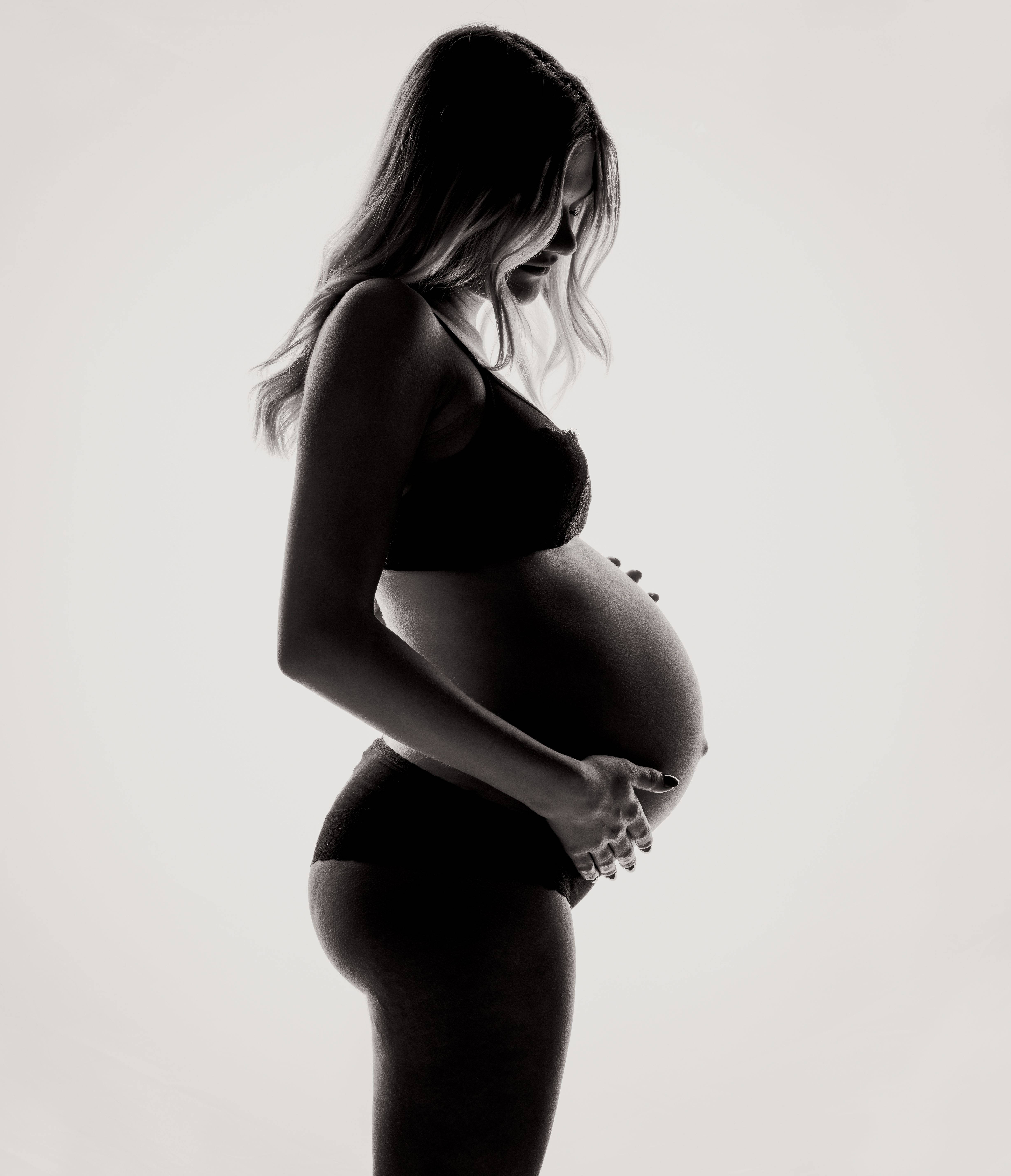 Pregnant 桌布 壁紙 — 一位孕婦剪影在柔和的白色背景前，溫柔地懷抱著腹部，呈現出一幅溫柔的黑白肖像。