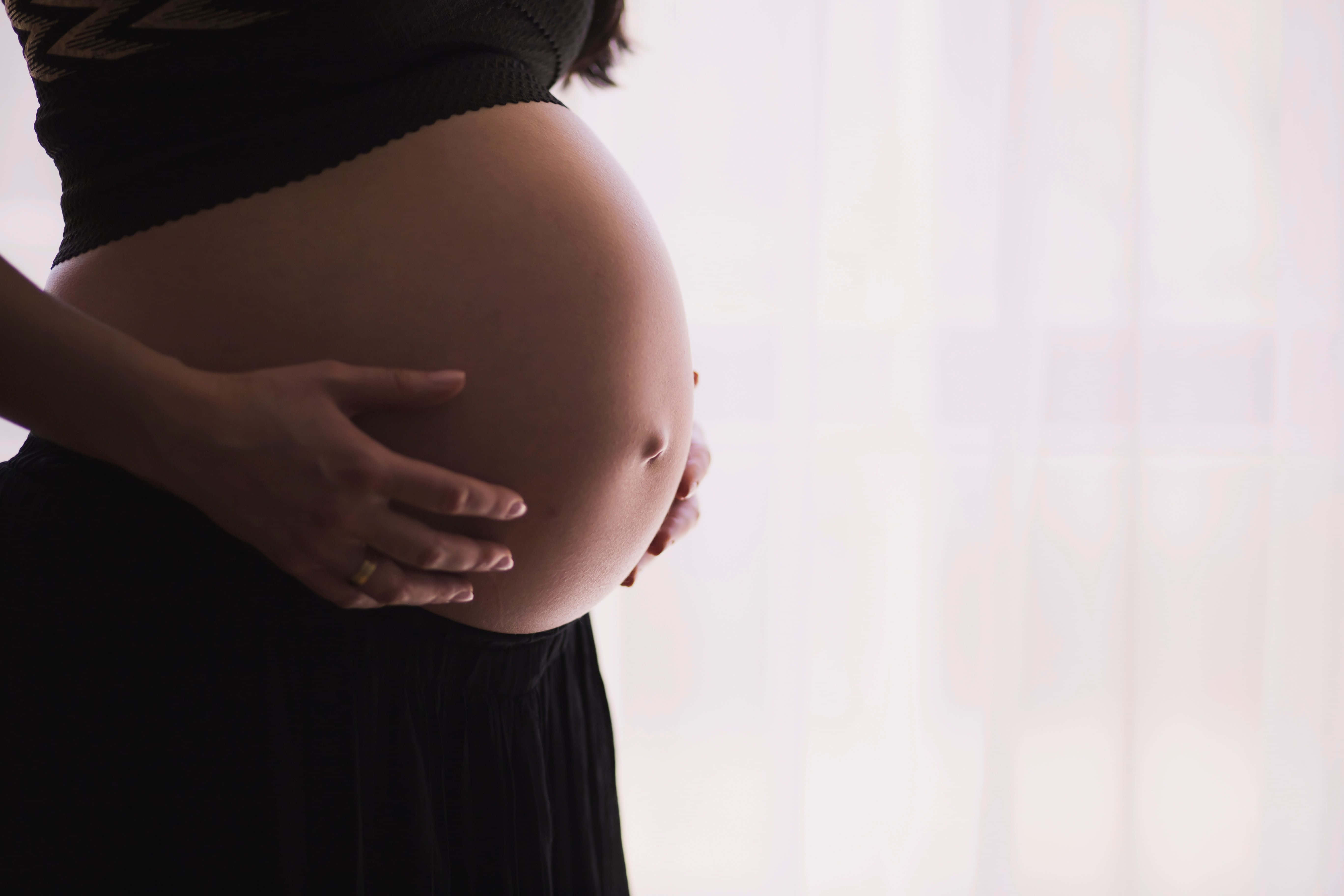 pregnancy 桌布 壁紙 — 一位孕婦在柔和模糊的窗戶背景下，輕輕地懷抱著她圓潤的腹部。