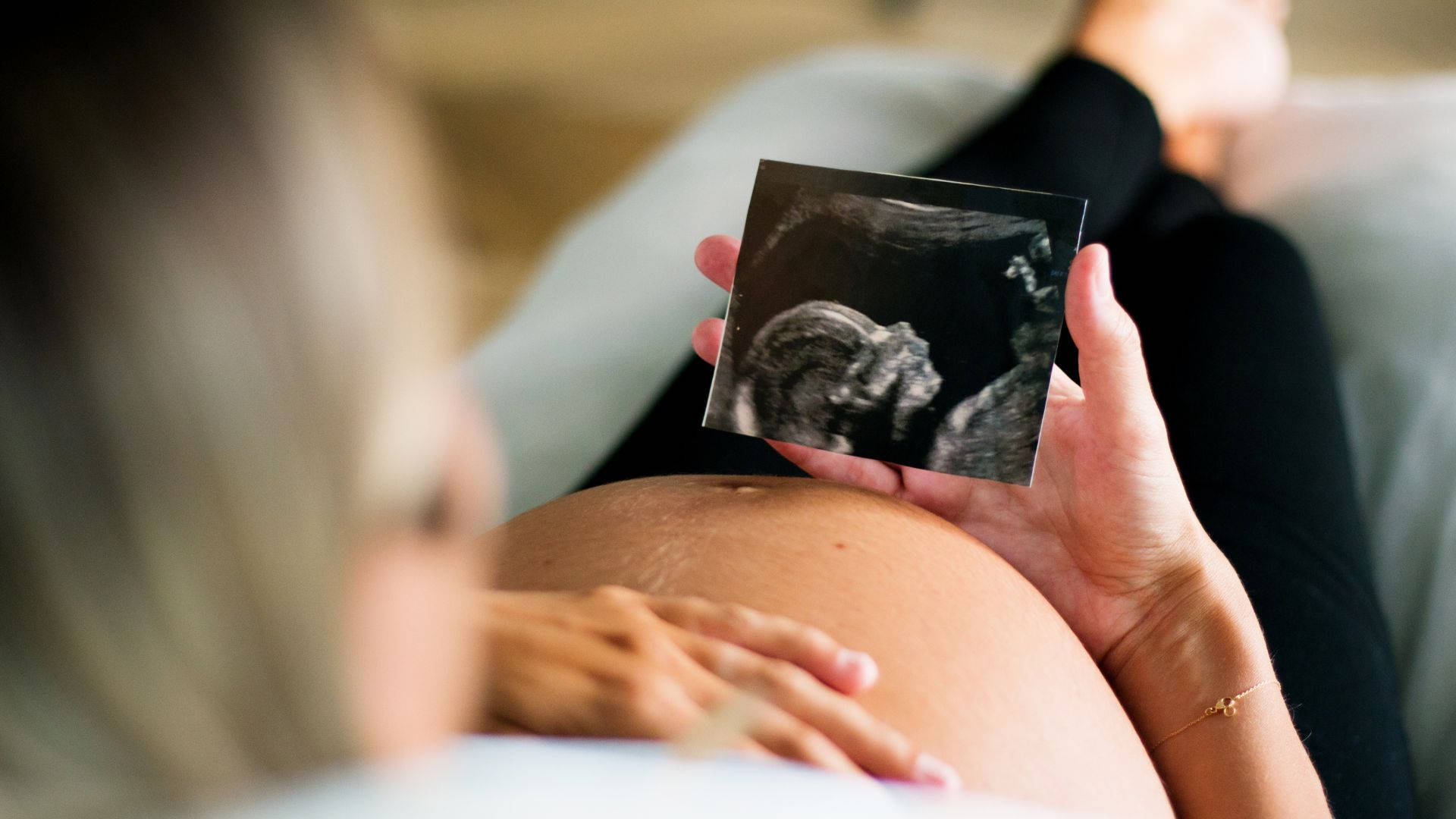 Pregnant 桌布 壁紙 — 一位孕婦在柔和自然光下，輕輕地將超音波照片放在肚子上方。