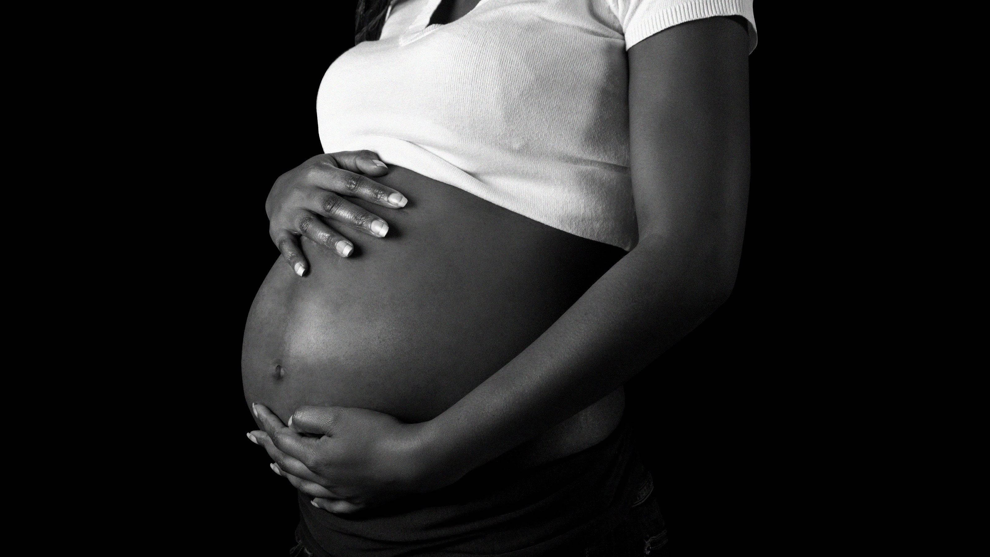Pregnant Belly 桌布 壁紙 — 一位孕婦在純黑背景下用雙手捧著腹部，呈現單色肖像。