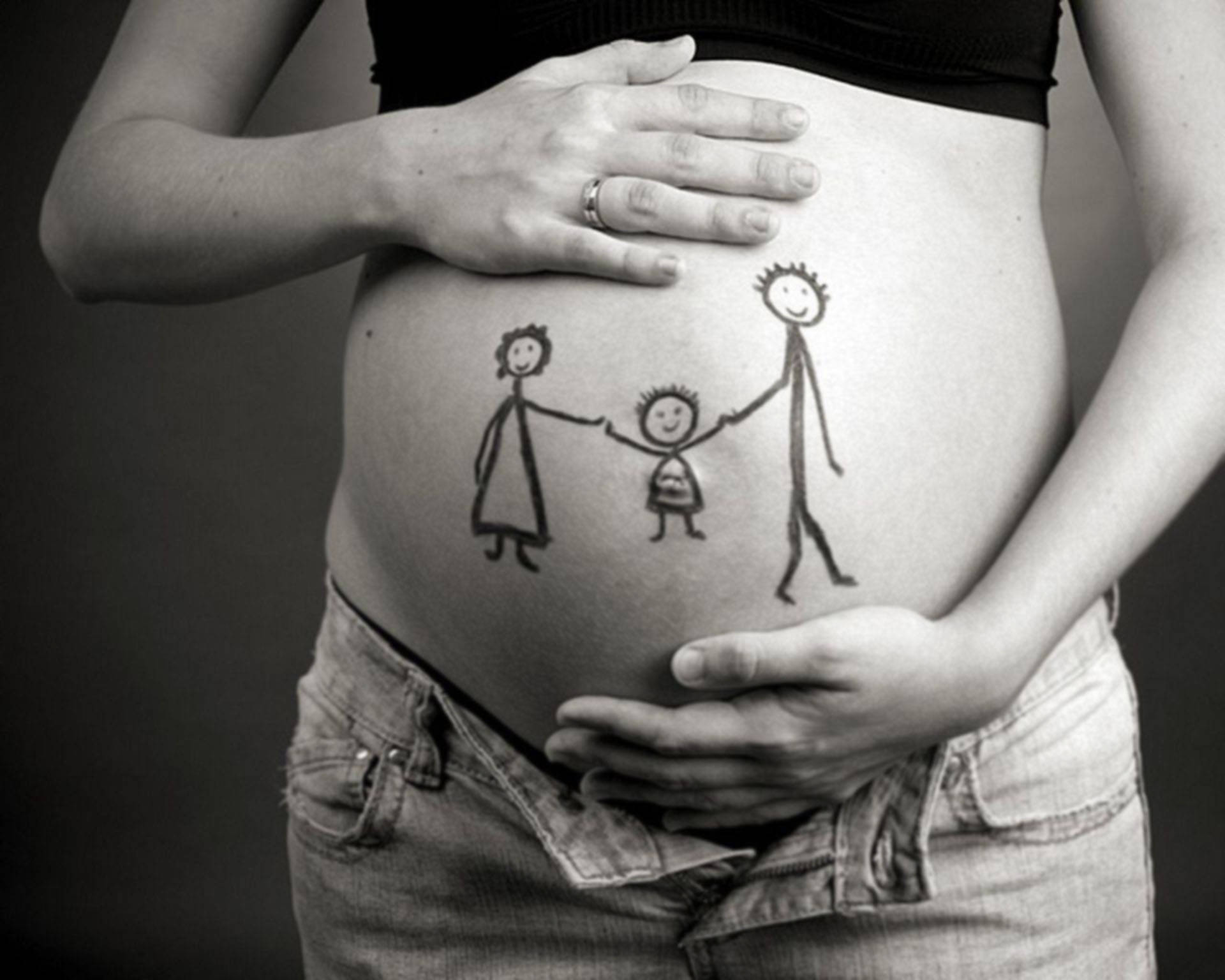 Pregnant 桌布 壁紙 — 一位孕婦的肚子上有一個孩子氣的畫，畫著三個火柴人牽手，她的雙手輕輕地捧著腹部。