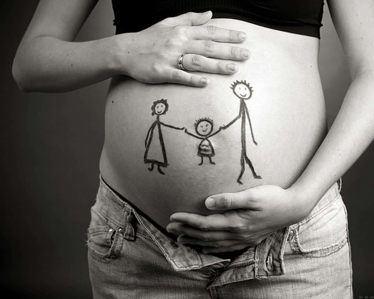 Pregnant 桌布 壁紙 — 一位孕婦的肚子上有孩子畫的一家三口手牽手的圖畫，被她的雙手輕輕捧著。