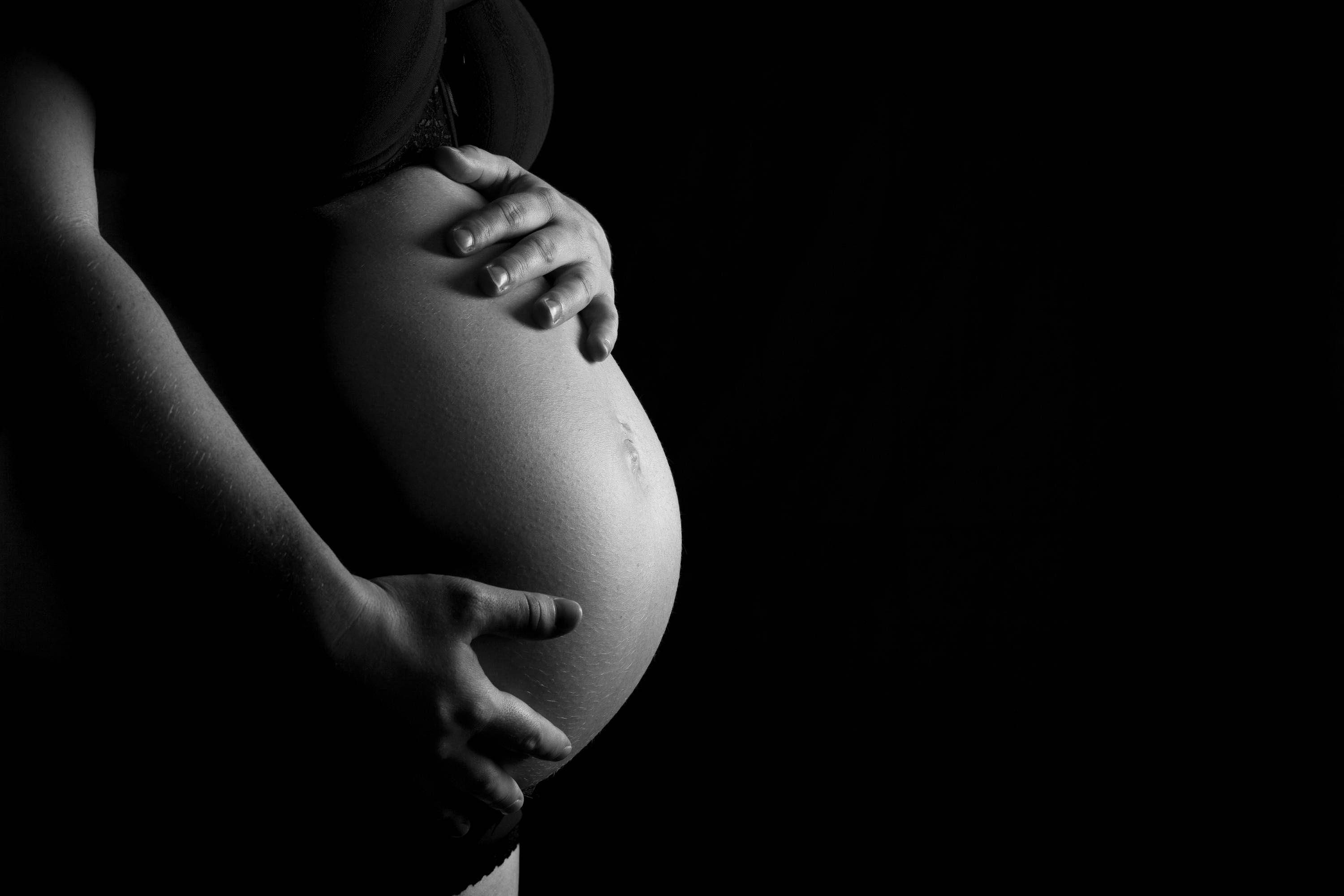 Pregnant Belly 桌布 壁紙 — 一位孕婦的雙手在黑色背景前，以黑白肖像照輕撫她圓潤的腹部。