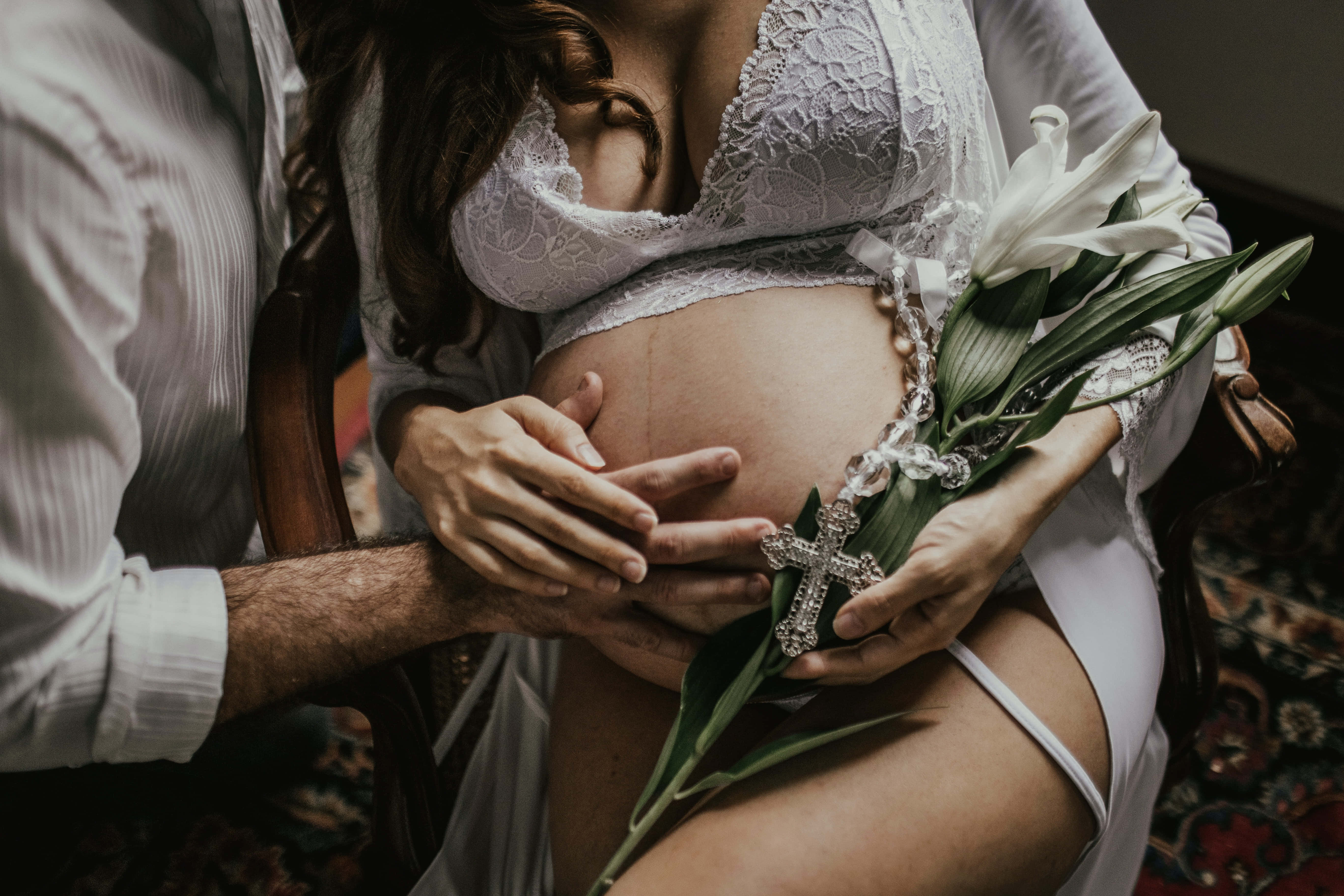 Pregnant 桌布 壁紙 — 一位孕婦穿著白色蕾絲內衣，用男人的手捧著腹部，同時手持白色百合花和水晶十字架。