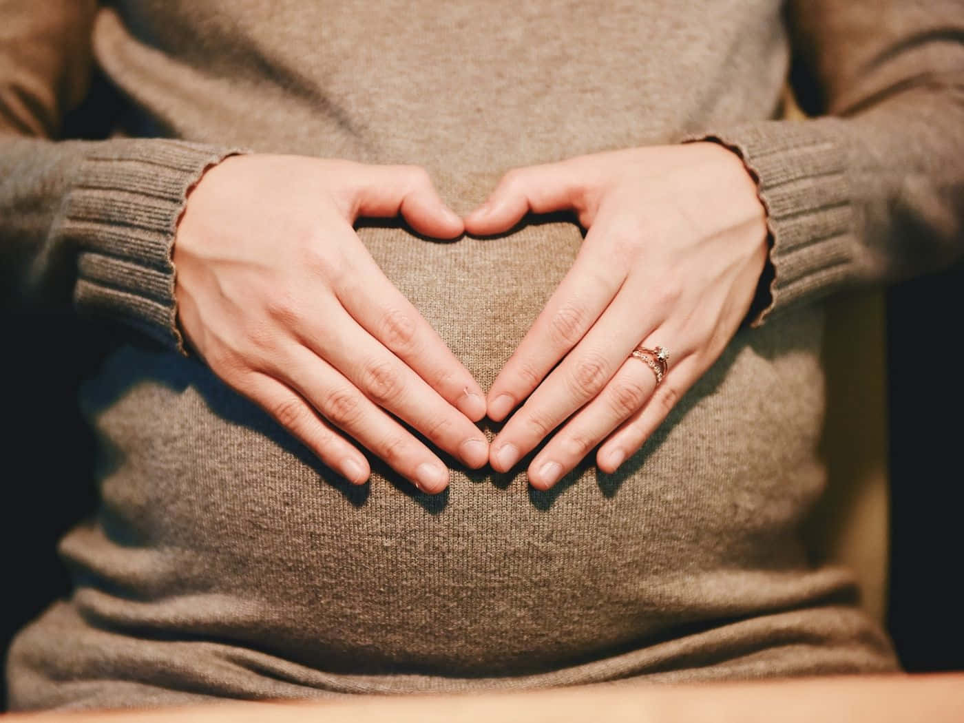 pregnancy 桌布 壁紙 — 一位孕婦穿著舒適的棕色毛衣，雙手輕輕在肚子上形成心形。