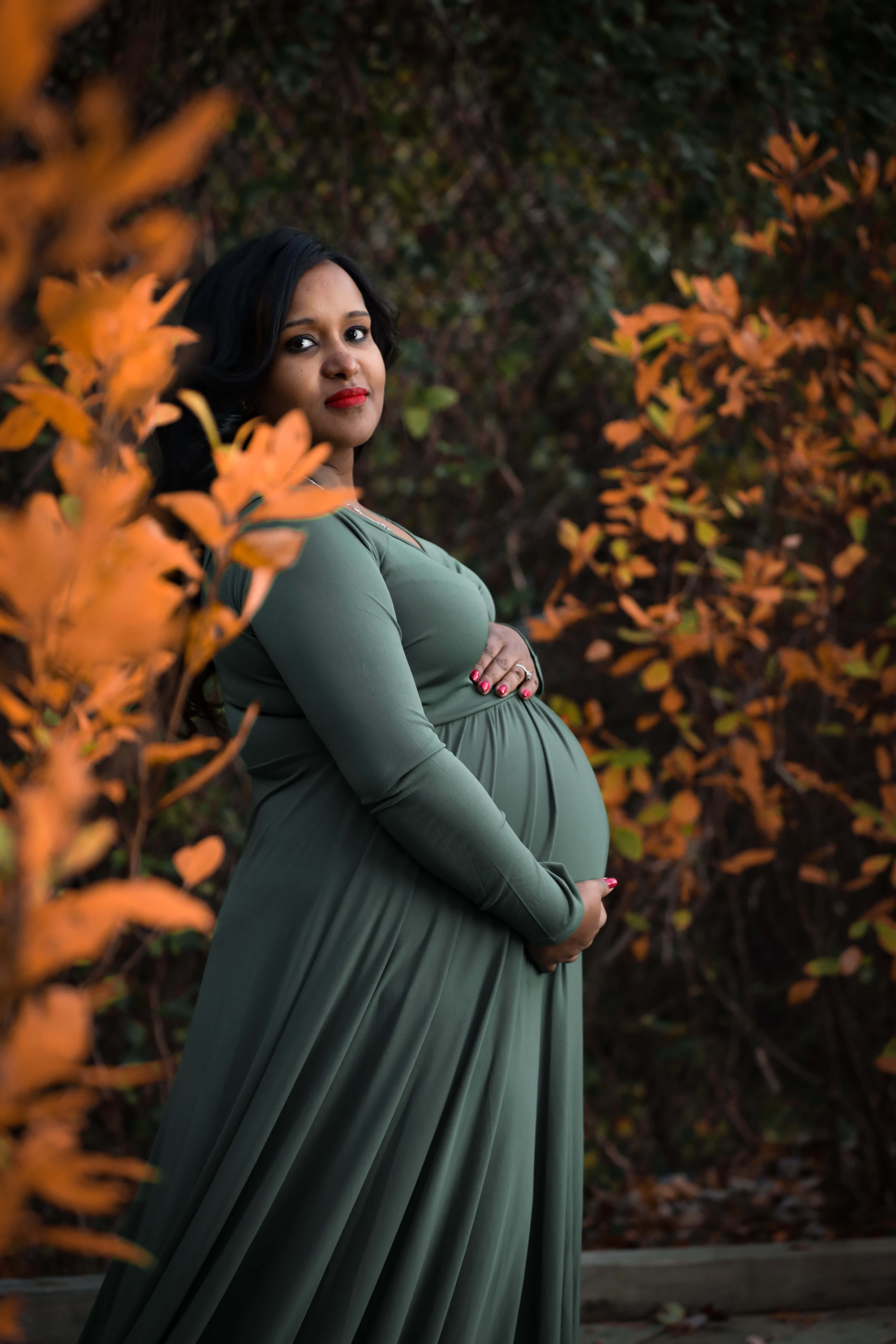 Pregnant 桌布 壁紙 — 一位孕婦穿著飄逸的綠色連衣裙，在充滿活力的橙色秋葉中輕輕地抱著肚子。