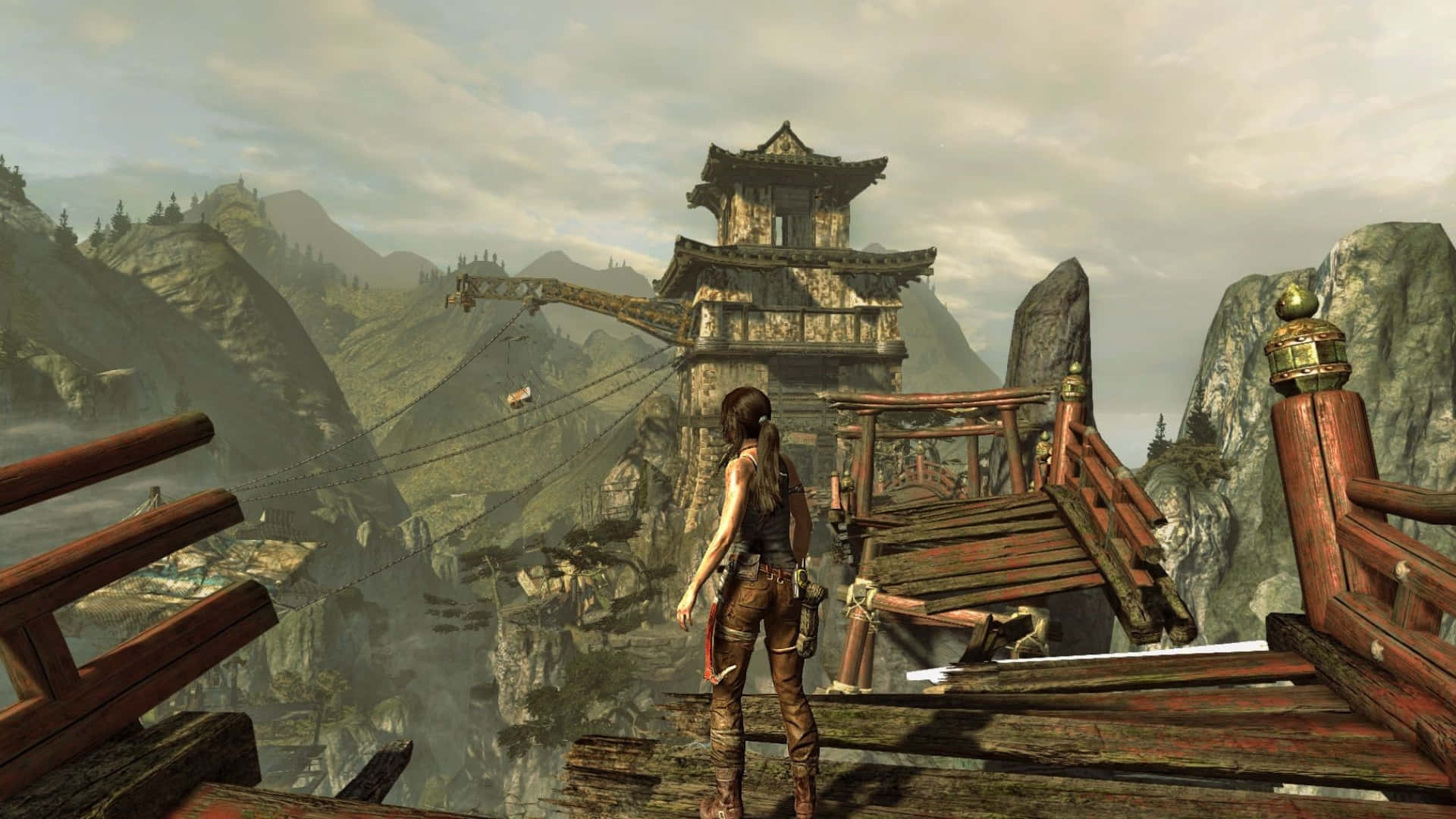 Lara Croft 桌布 壁紙 — 一位孤獨的冒險家站在一座風化的木橋上，俯瞰著霧氣瀰漫的山谷，遠處有一座古老的亞洲風格塔樓。