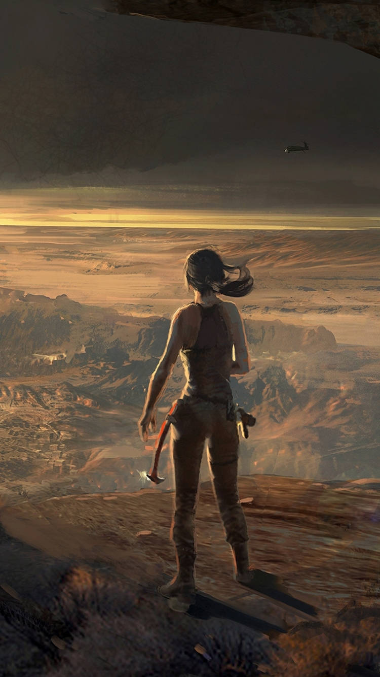 tomb raider iPhone 桌布 壁紙 — 一位孤獨的冒險家站在懸崖邊緣，俯瞰廣闊的沙漠峽谷，正值黃金時刻，遠處可見一架直升機。